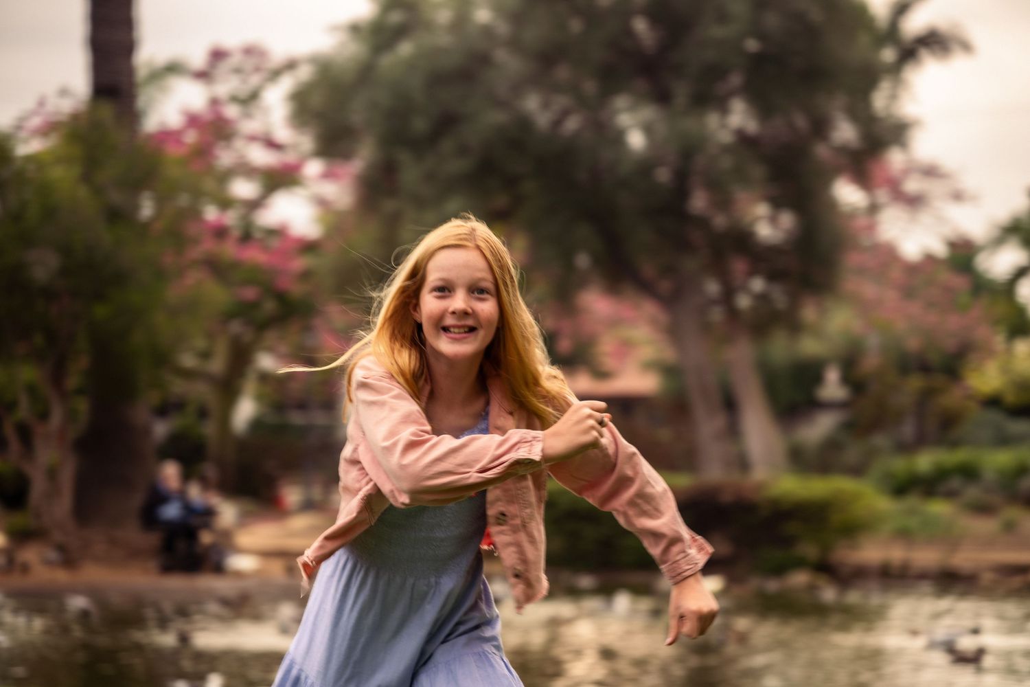 Editorial documentary family moment of a child running toward parents in a sunny park with trees, greenery, and soft natural light.