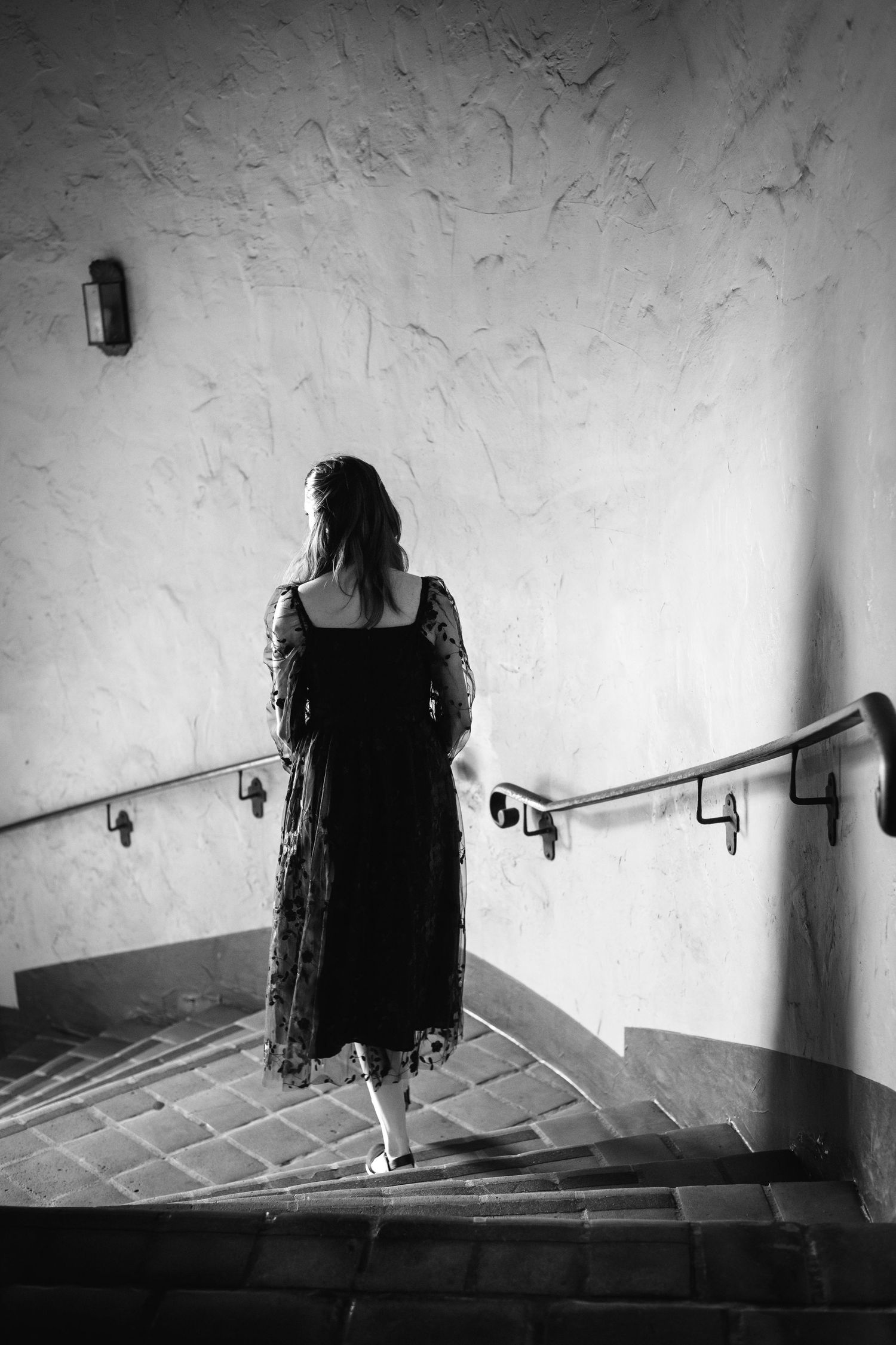 Romantic editorial documentary moment of a woman descending a curved stairwell in black and white with elegant shadows and texture.