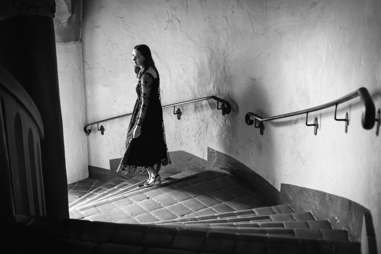 Natural editorial documentary wedding moment of a bride by carved stone columns in soft black‑and‑white Santa Barbara courthouse light.
