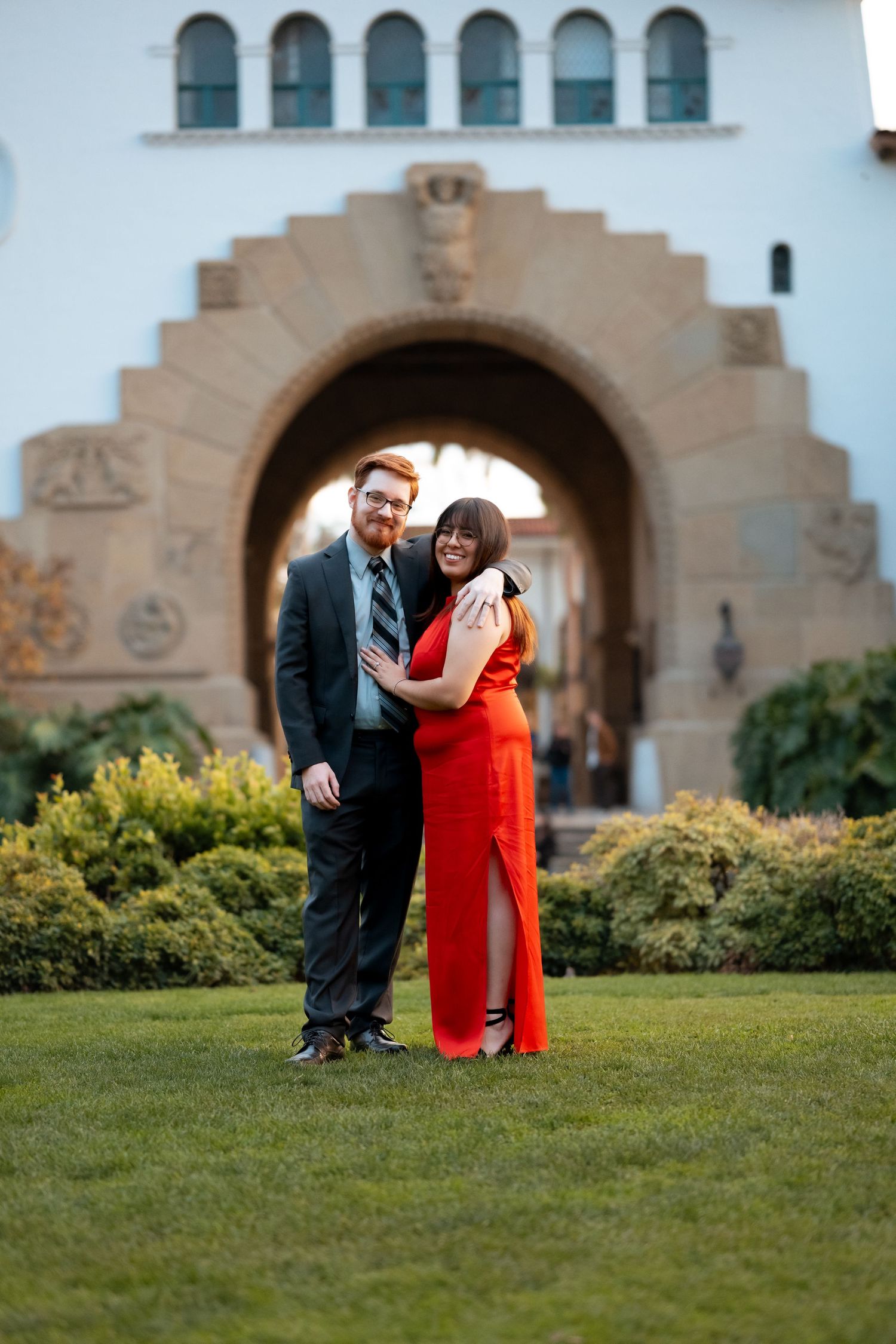 Natural editorial documentary wedding moment of a couple standing together on a lawn in front of a grand stone building with arched details.