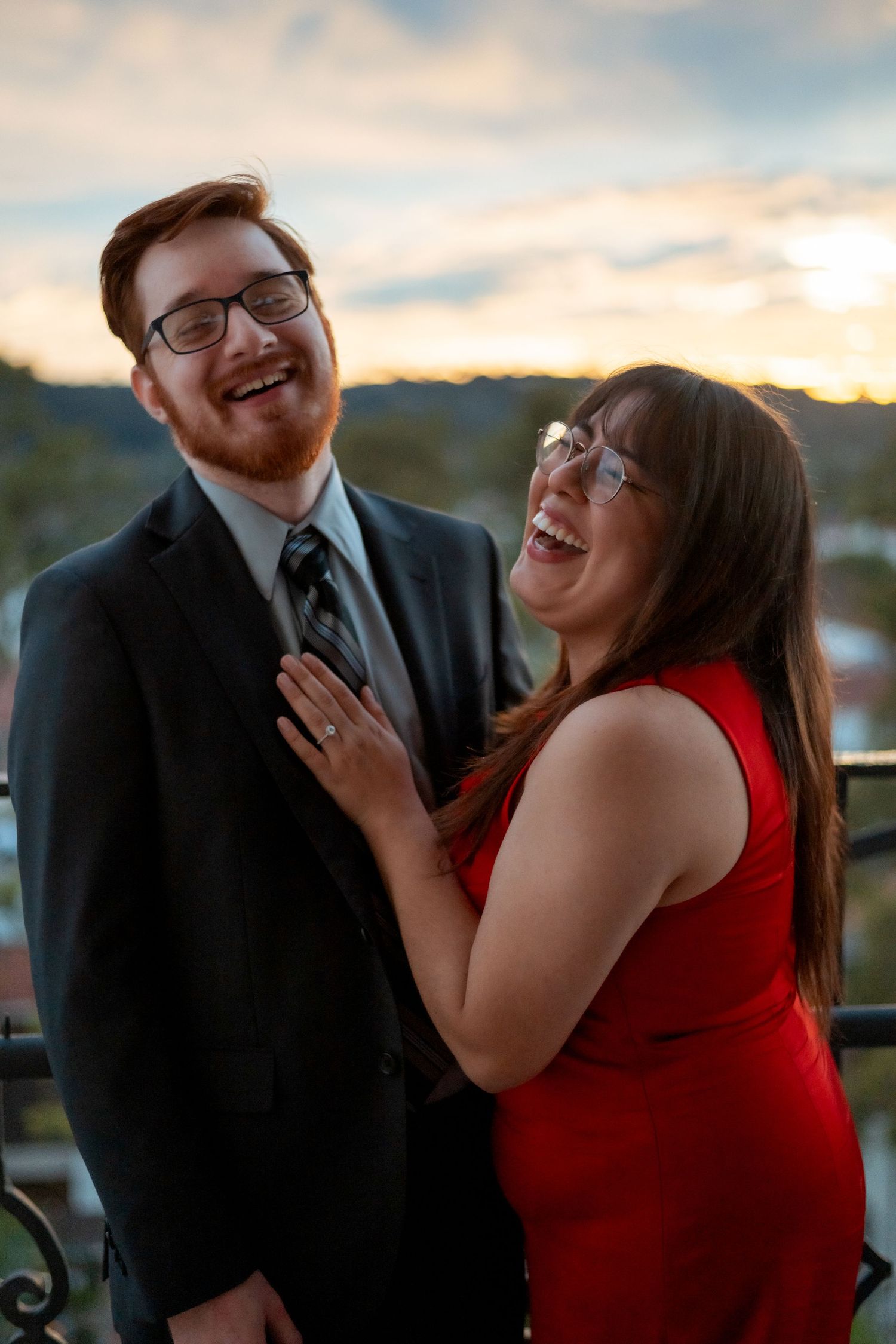 Natural editorial documentary elopement moment of a couple laughing together at sunset with hills, trees, and warm golden light behind them.
