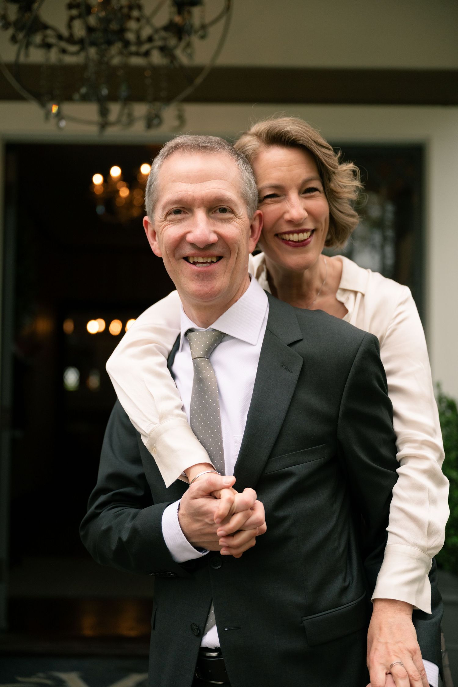 Natural editorial documentary wedding moment of a couple standing close in a doorway with warm indoor light behind them.