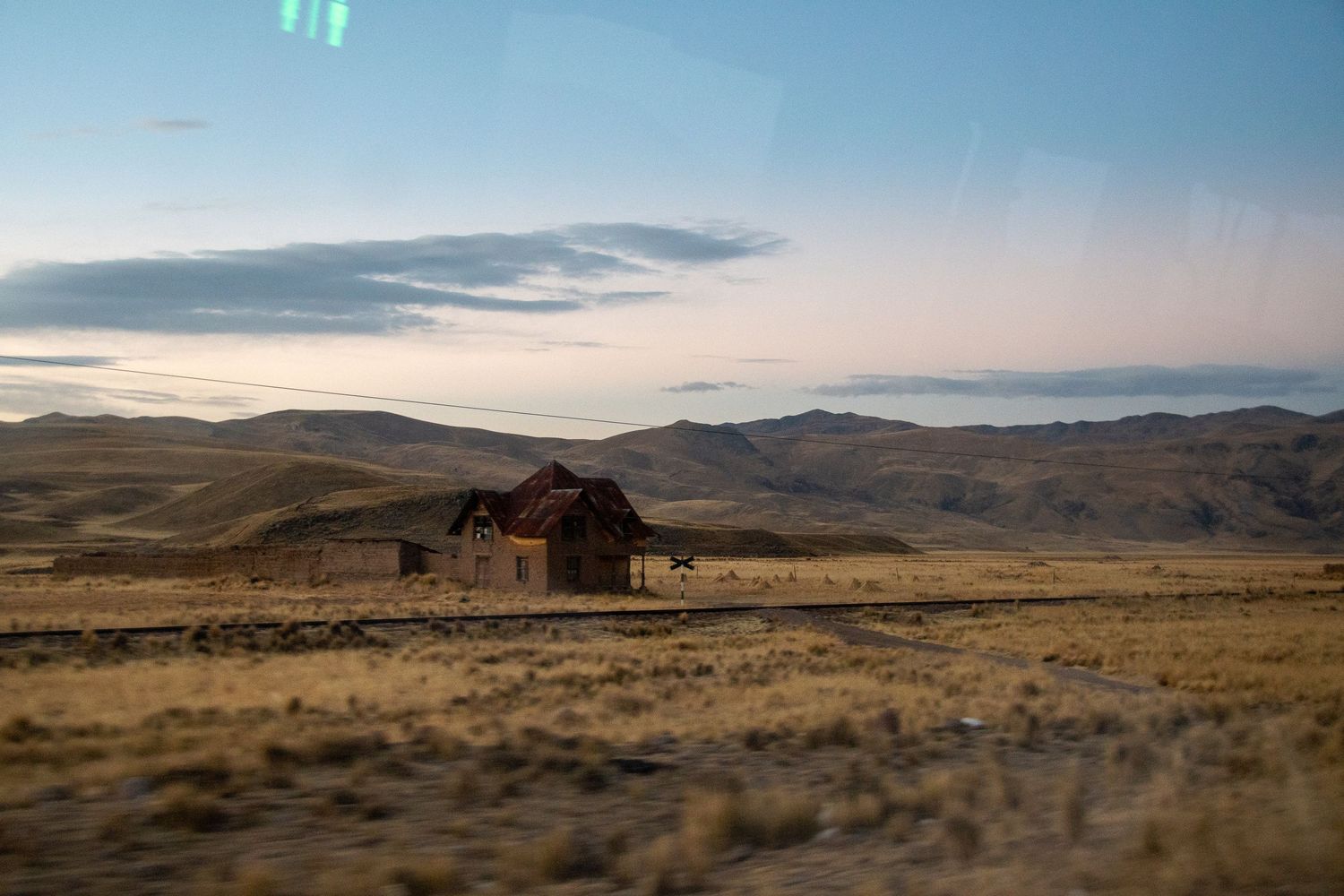 Romantic editorial documentary scene of an old rural building in golden grass at dusk with soft sky tones and quiet open space.