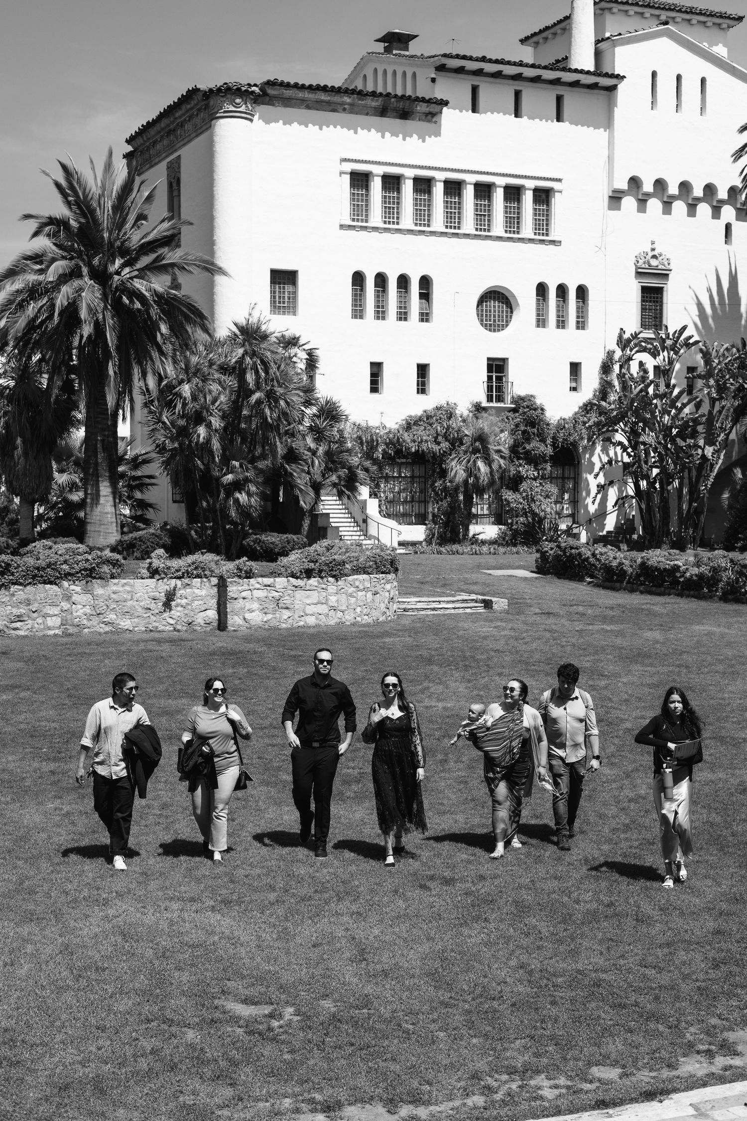 Natural editorial documentary Santa Barbara courthouse wedding moment of a group walking across the lawn in timeless black and white.