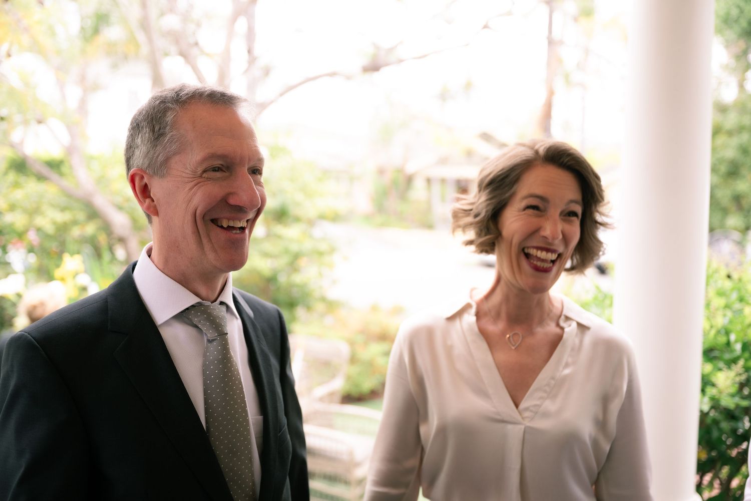 Natural editorial documentary wedding moment of two adults talking outdoors with greenery and bright light around them.
