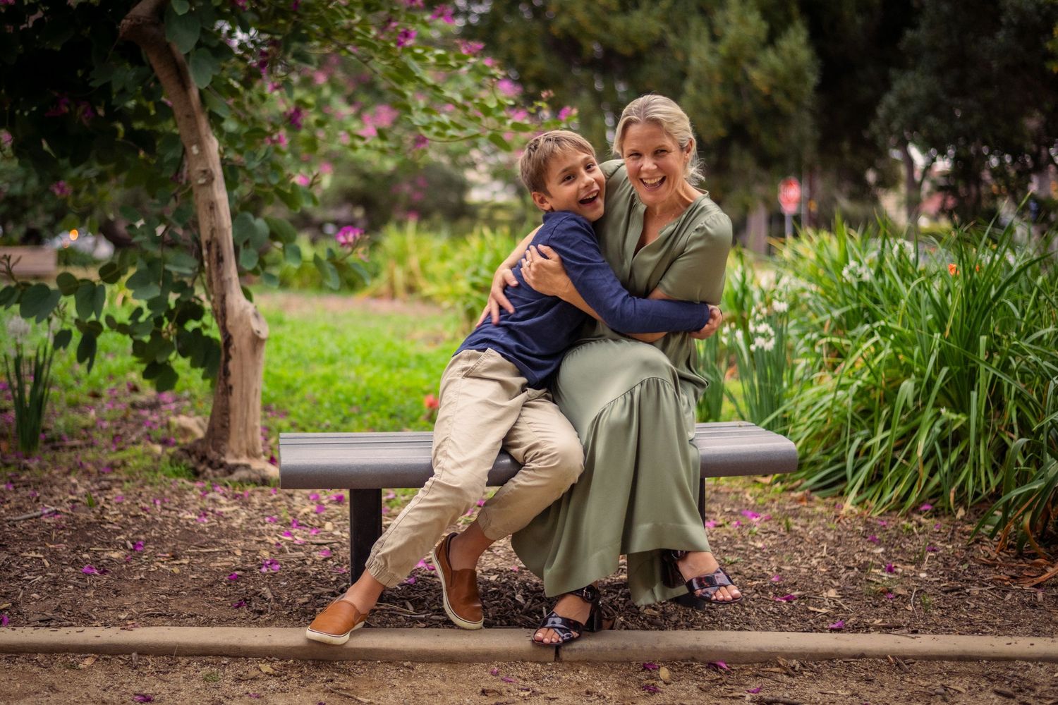 Editorial documentary moment of a mom and son hugging on a garden bench surrounded by greenery, flowers, and soft natural light.