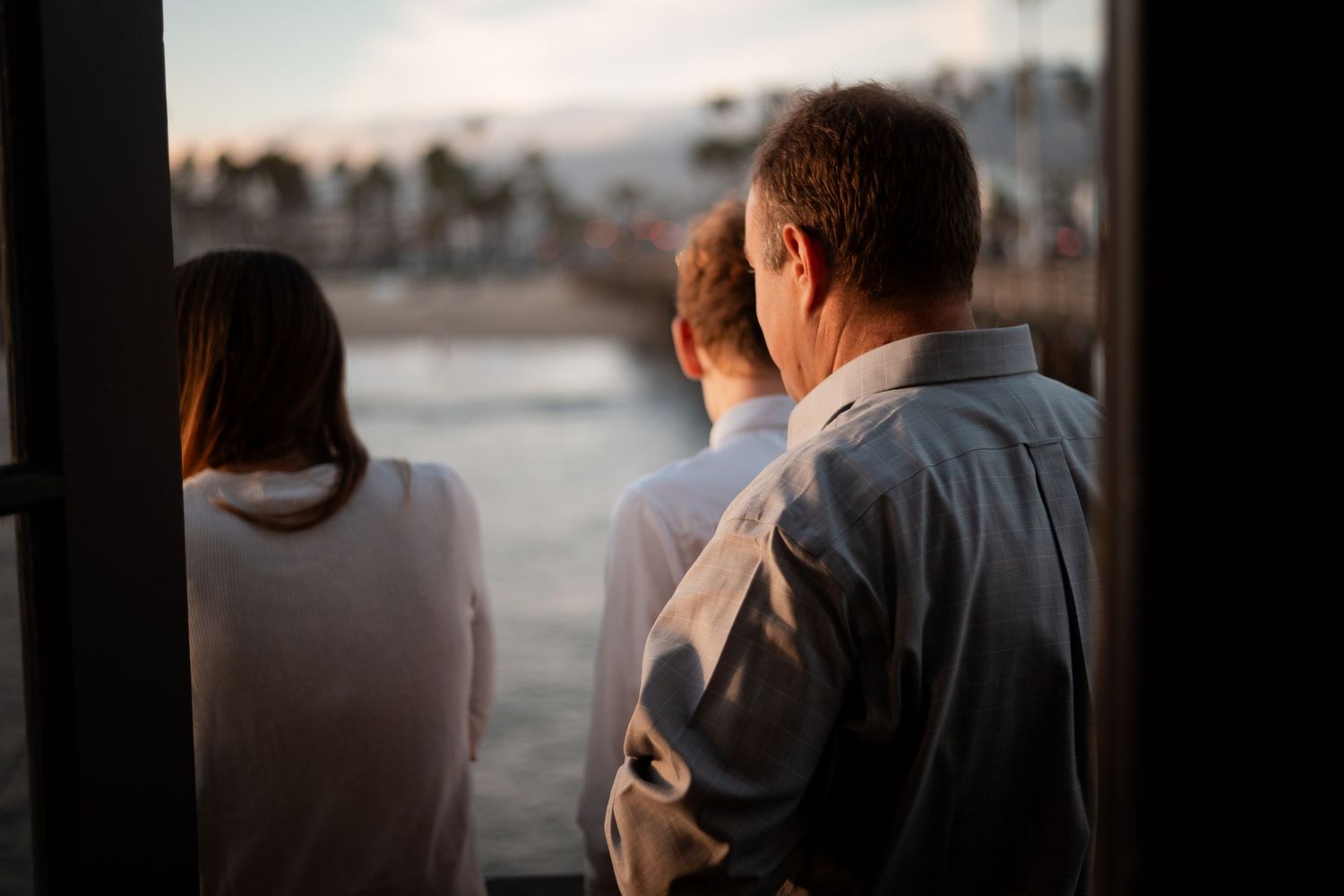 Natural editorial documentary wedding moment of a group standing together by the water at sunset, sharing a quiet, warm scene.