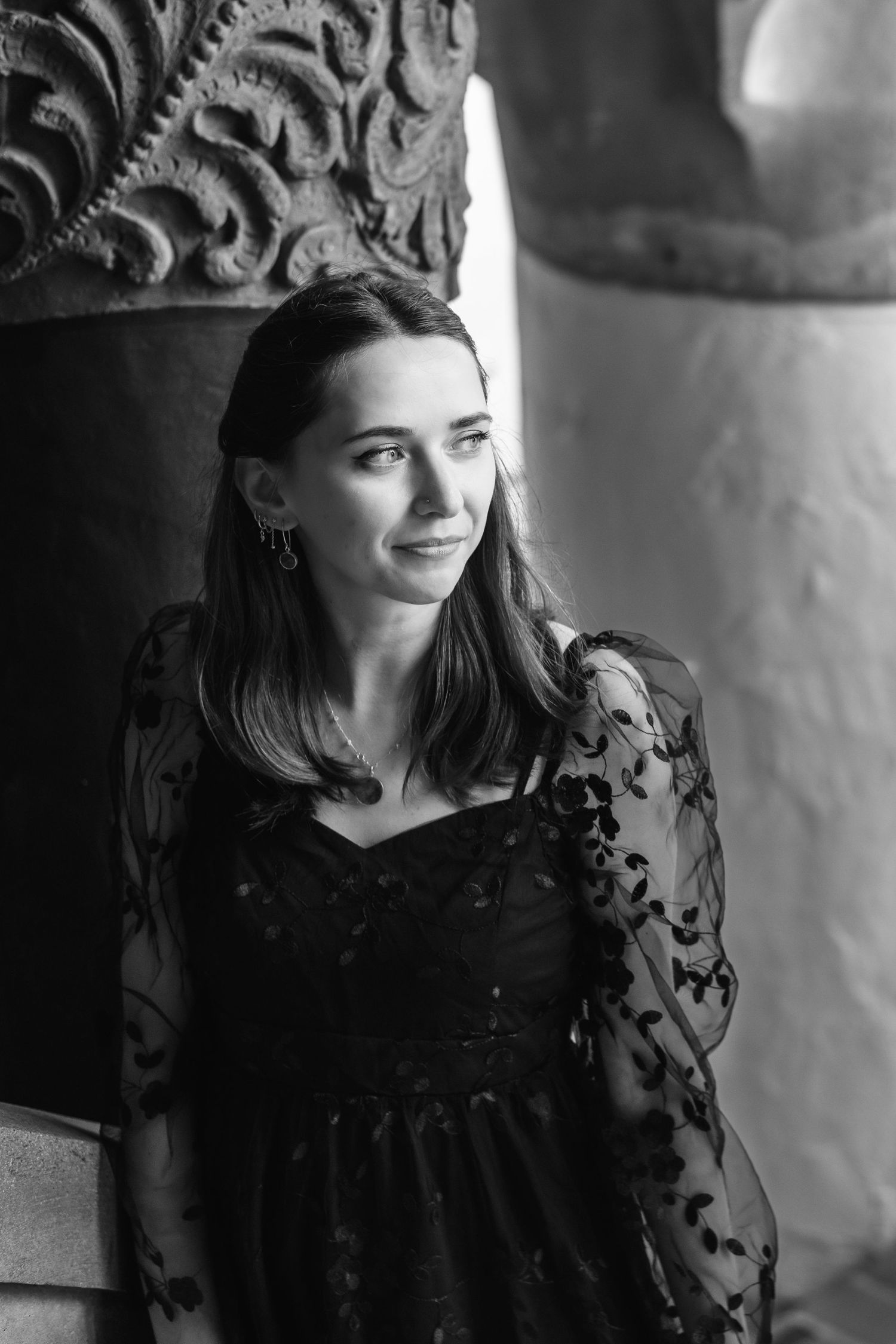 Natural editorial documentary wedding moment of a bride by carved stone columns in soft black‑and‑white Santa Barbara courthouse light.
