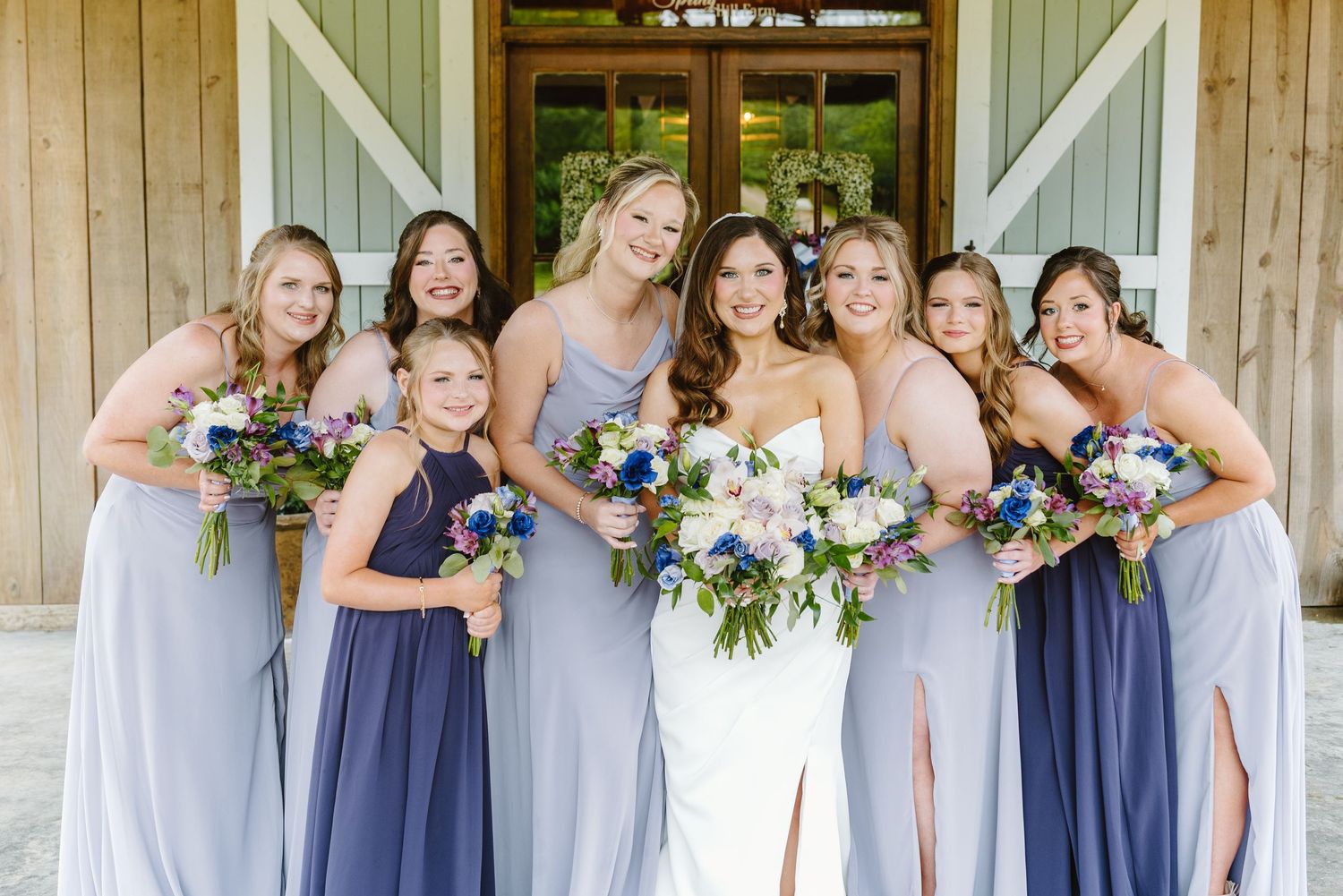 Bridesmaids in coordinating blue dresses pose together holding floral bouquets.