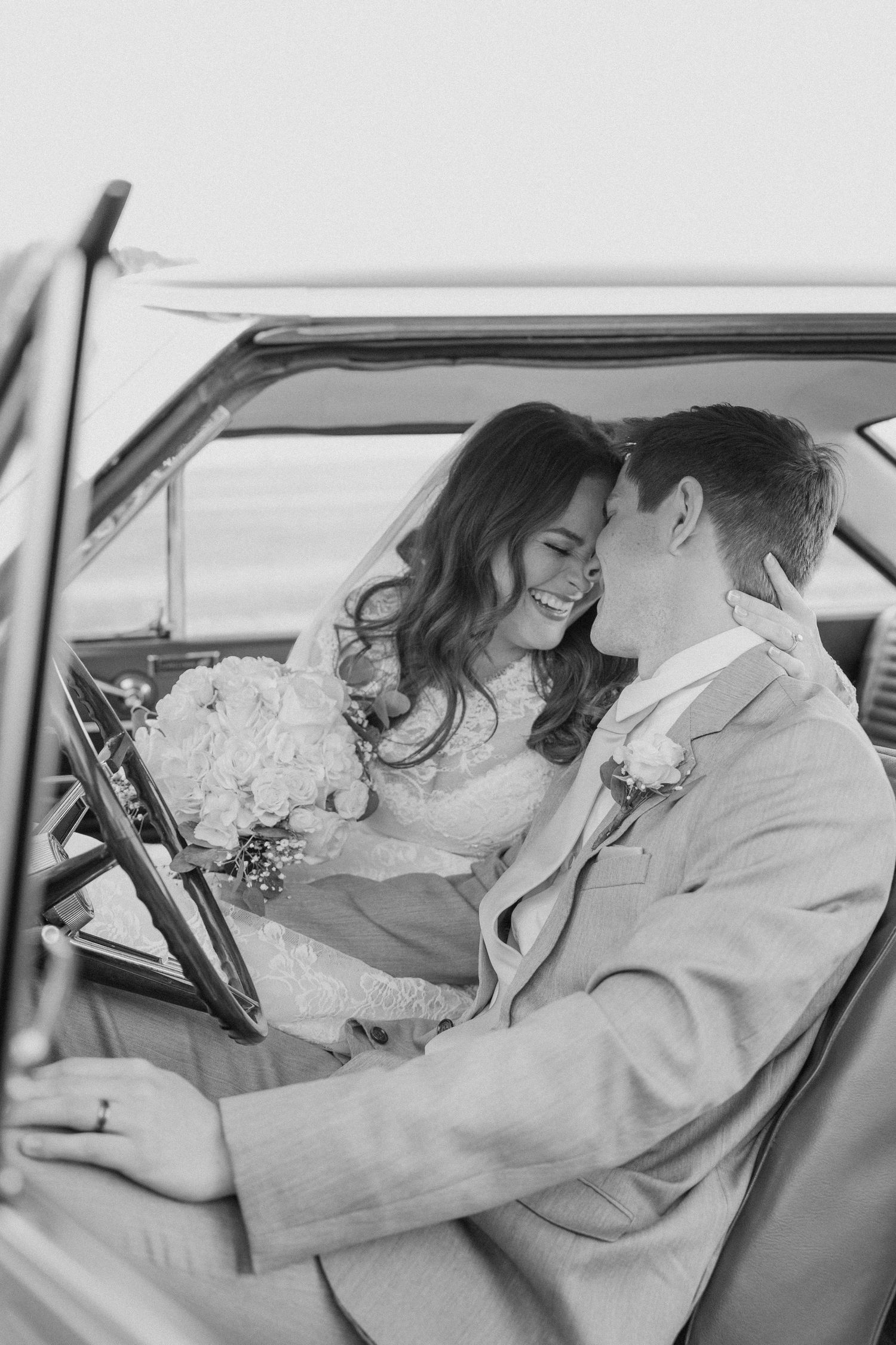 Black and white photo of a romantic moment between newlyweds in a classic car.