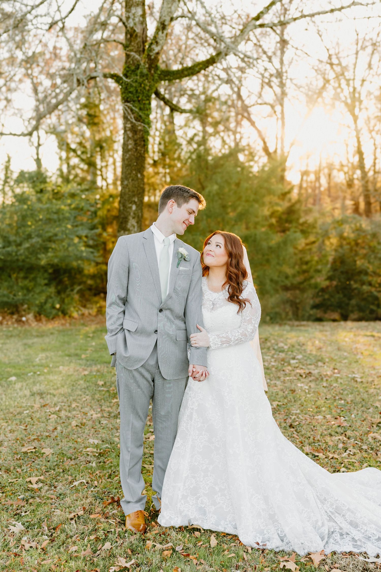 A couple in wedding attire poses together on fallen autumn leaves.