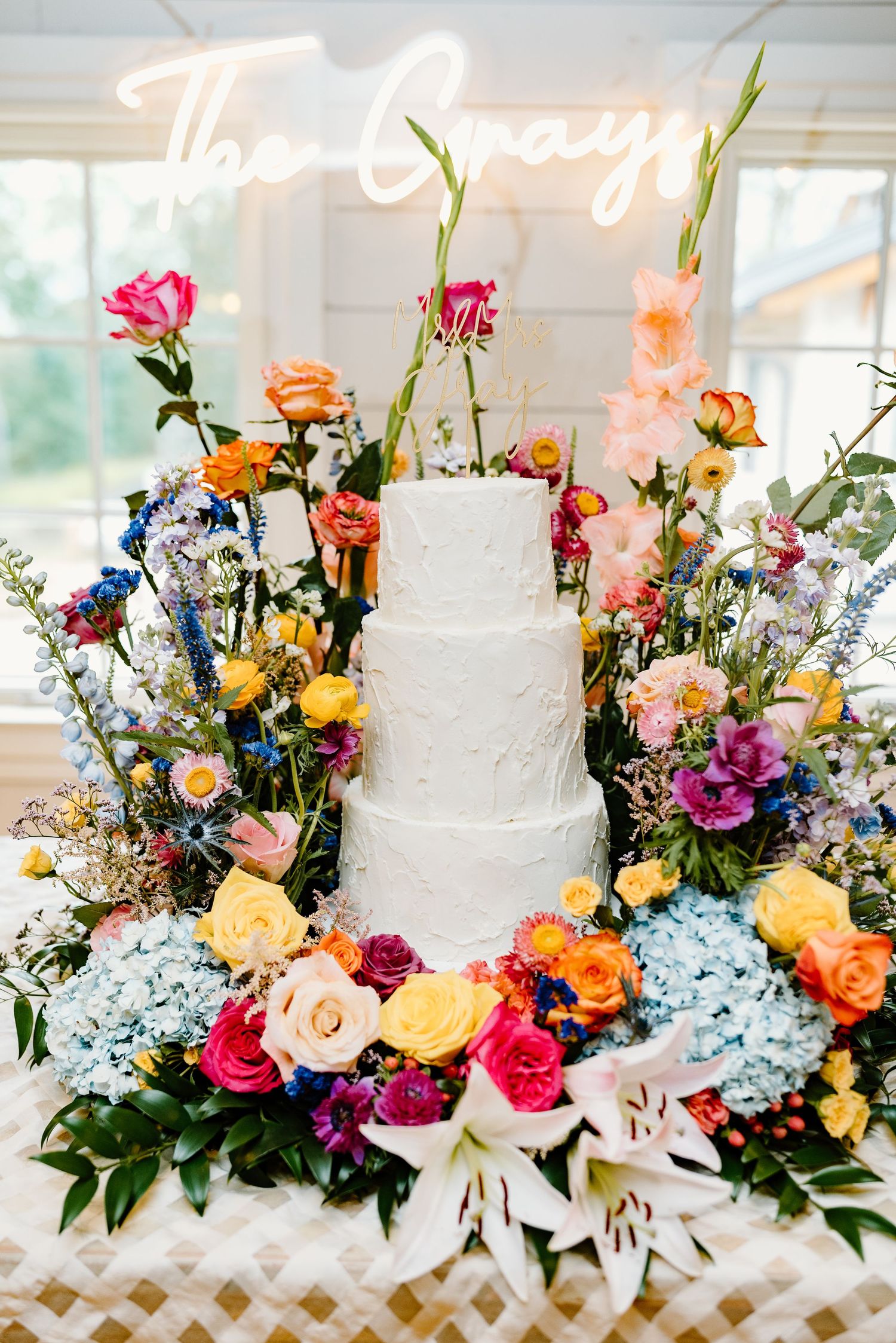 Colorful wedding floral arrangement featuring roses, hydrangeas, and mixed blooms on white lattice backdrop.