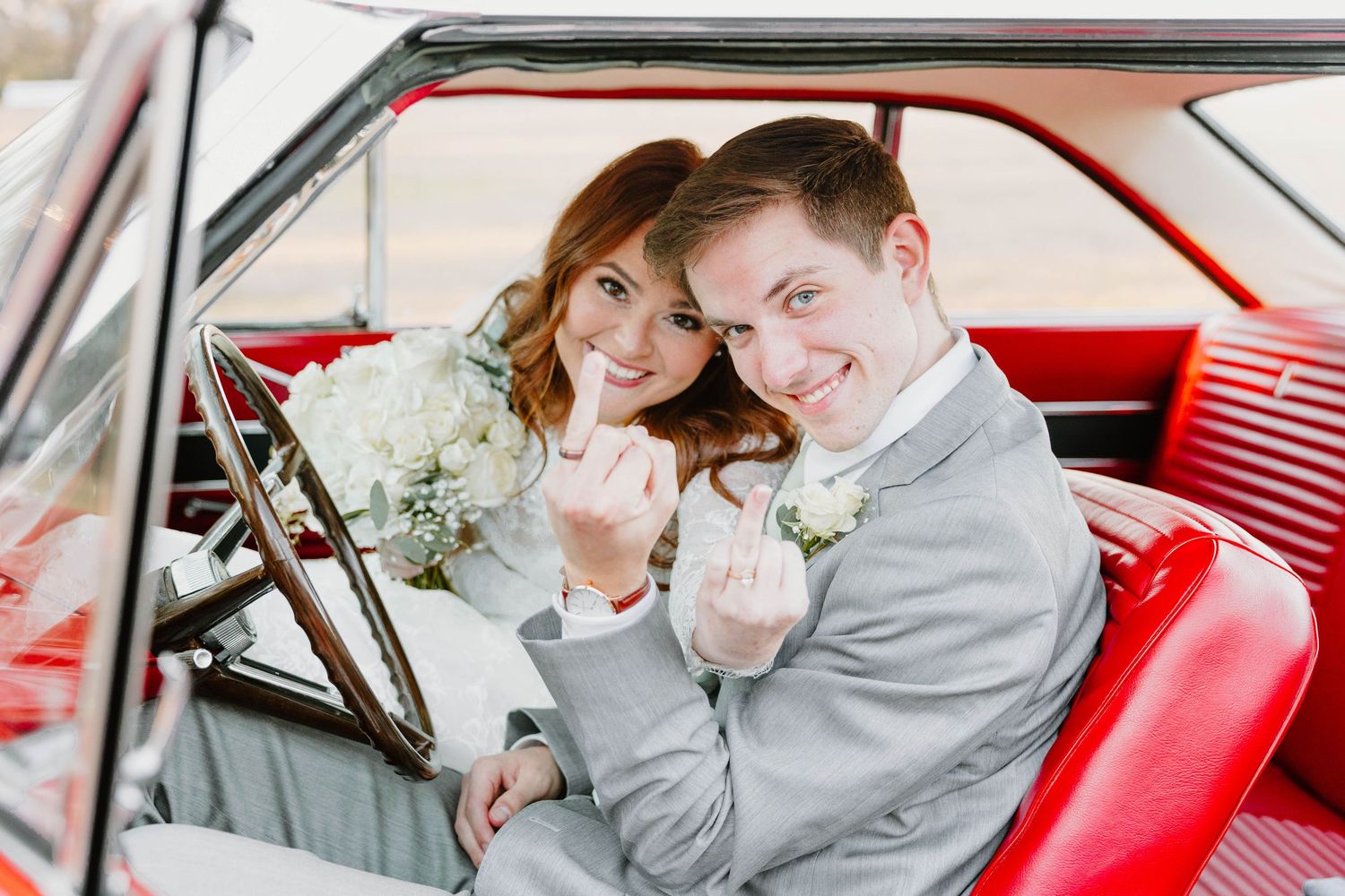 A couple shares an intimate moment inside a classic red vintage car.