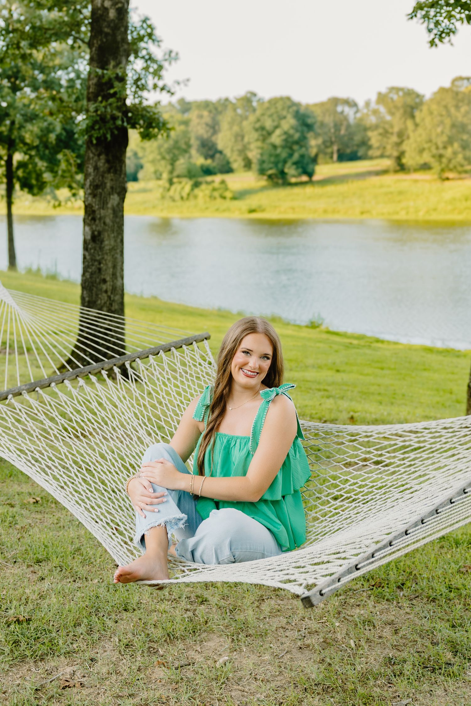 Person relaxing in a white hammock by a serene lake on a sunny summer afternoon.