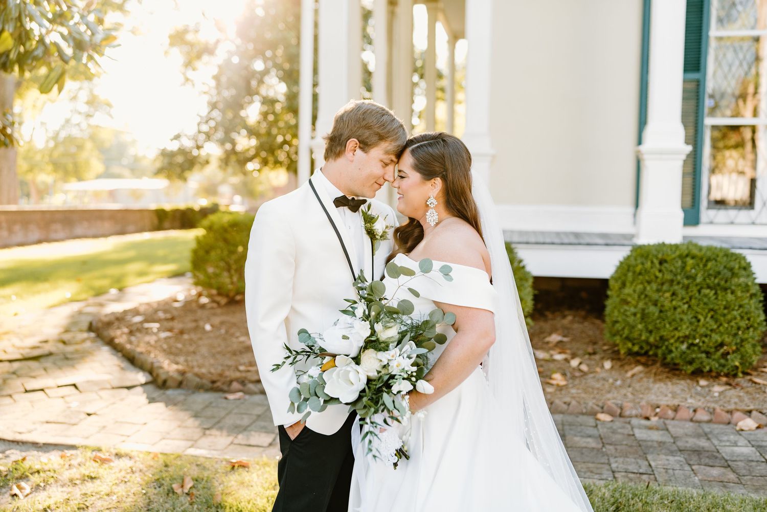 Elegant outdoor wedding portraits with white columns and natural greenery in background.