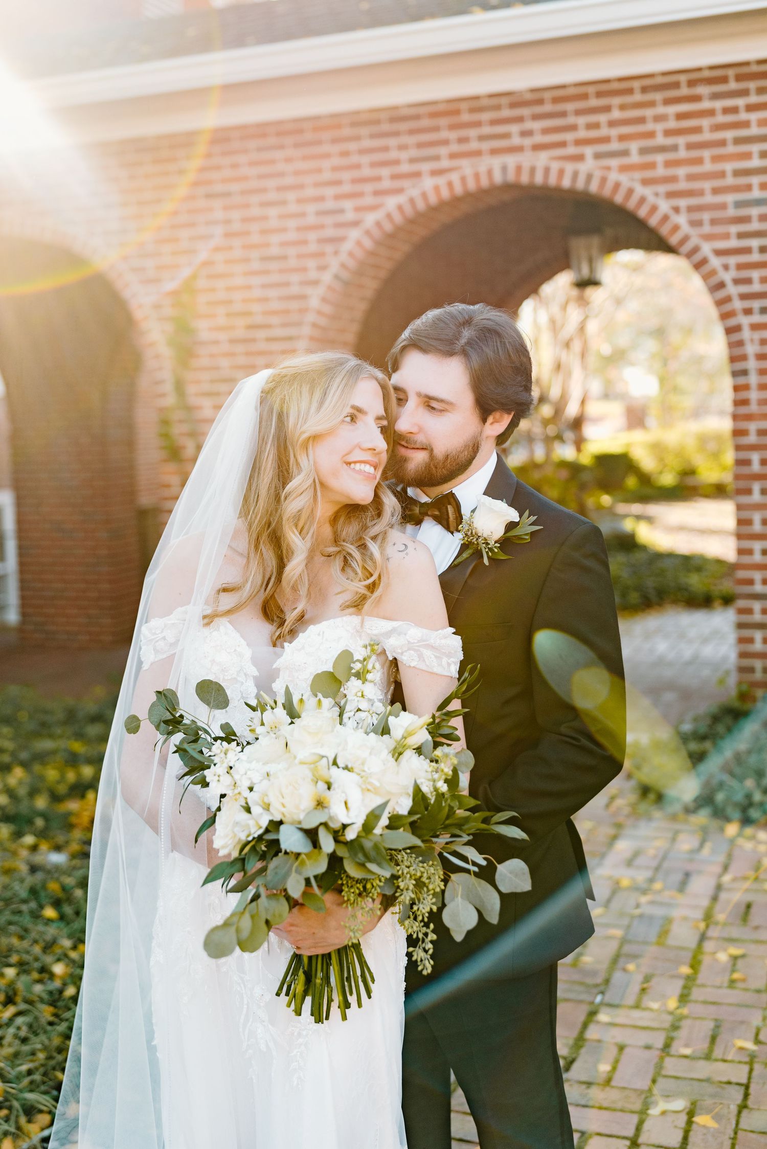 Romantic wedding portraits featuring white floral bouquets against a brick backdrop.