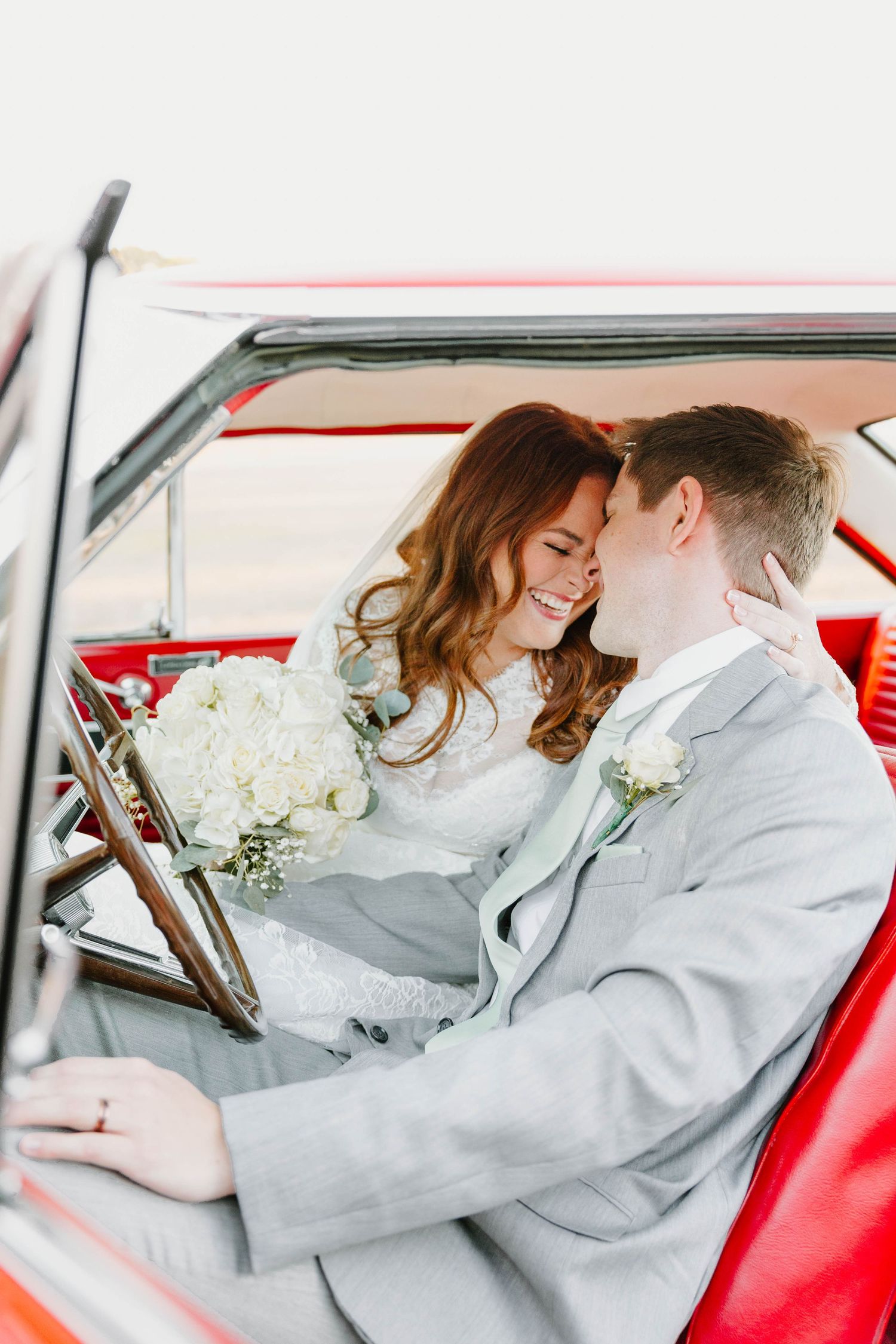 Couple sharing a romantic moment in a vintage red car with white flowers on wedding day.
