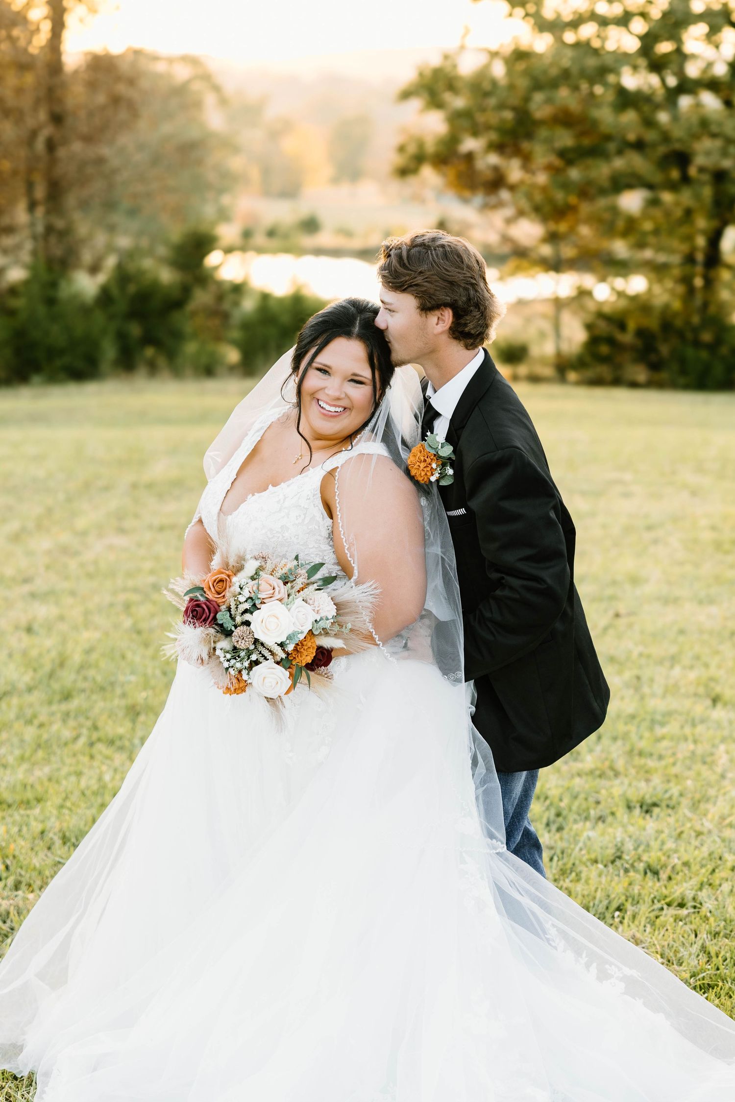 A couple in wedding attire embraces in a sun-drenched field during golden hour.