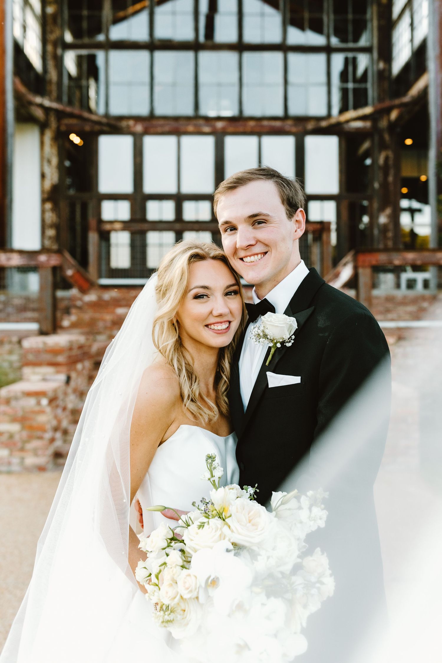 Wedding couple poses together in front of industrial-style windows with exposed brick.
