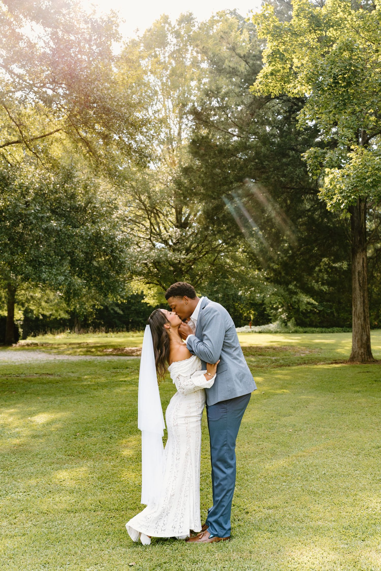 Romantic outdoor photoshoot in a sunlit garden with lush green trees creating a natural backdrop.