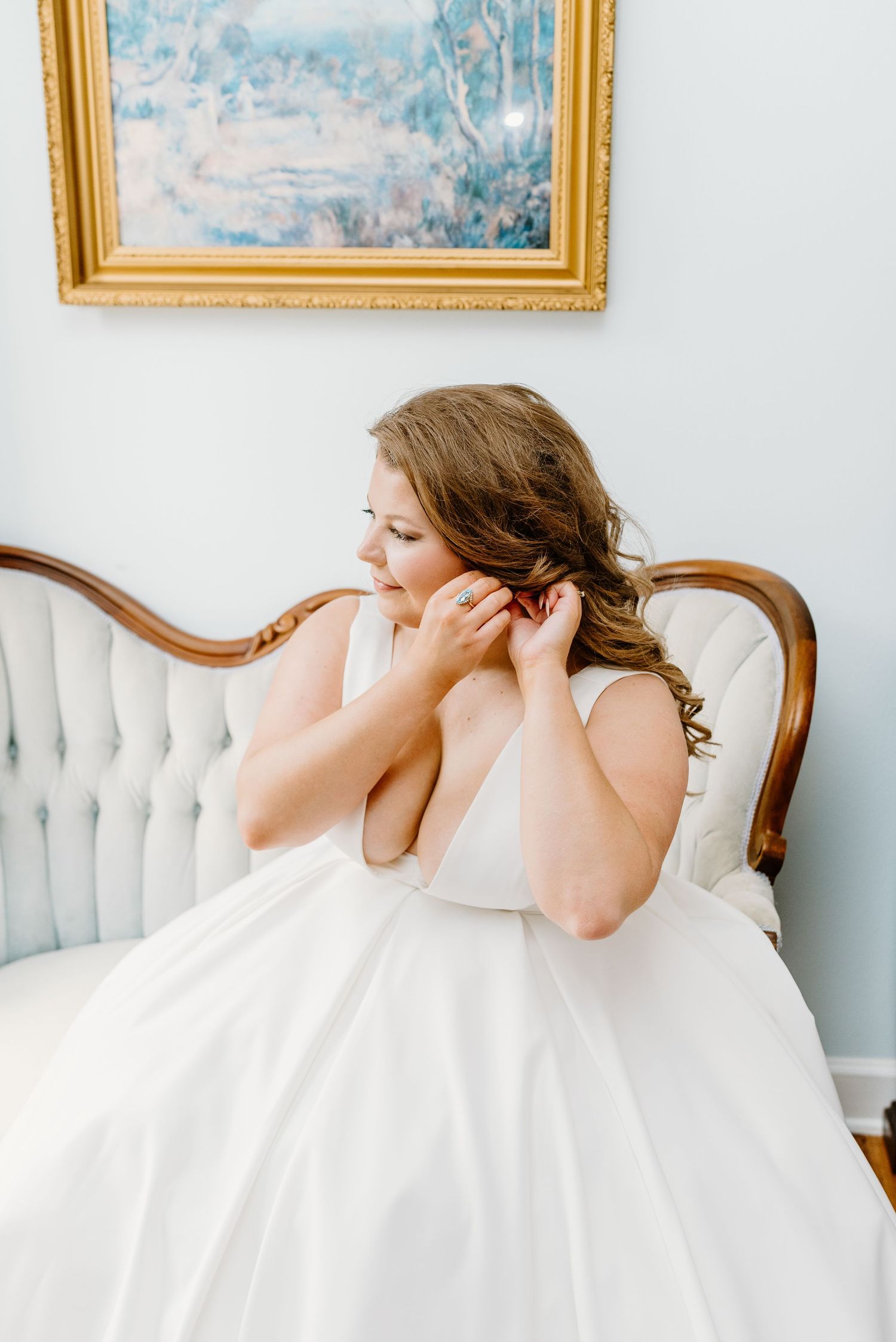 Woman in white dress reclining on vintage tufted sofa with gold-framed artwork in background.