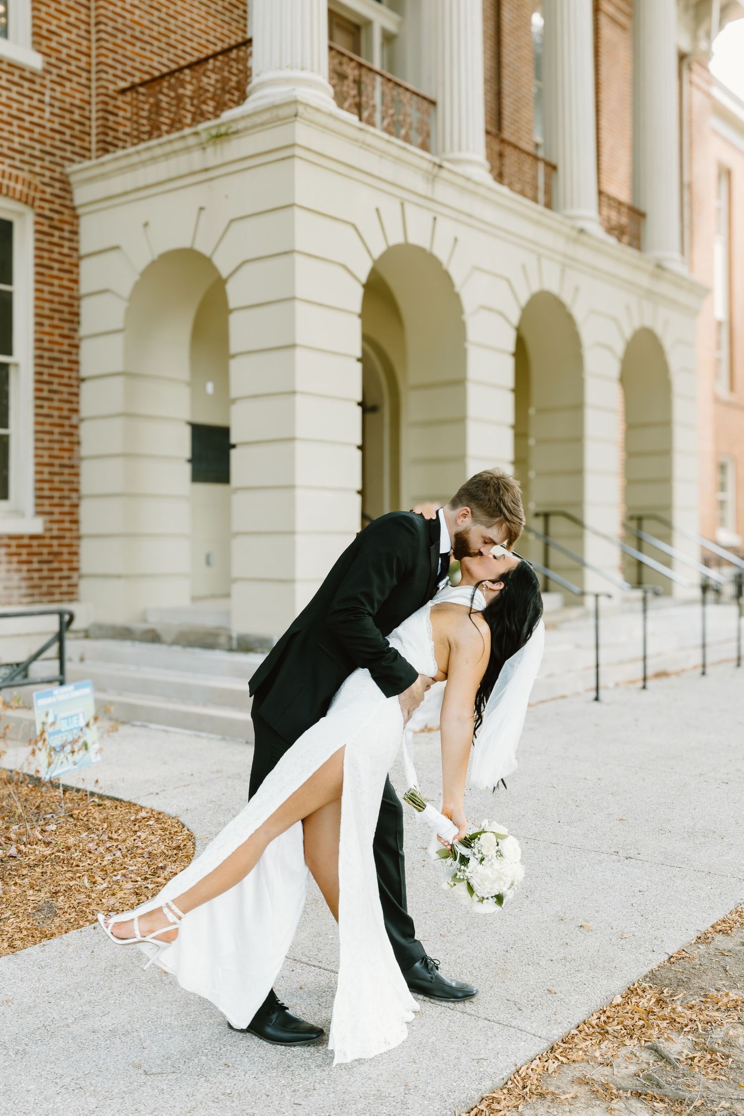 Romantic dip pose in front of classic brick and white column architecture.
