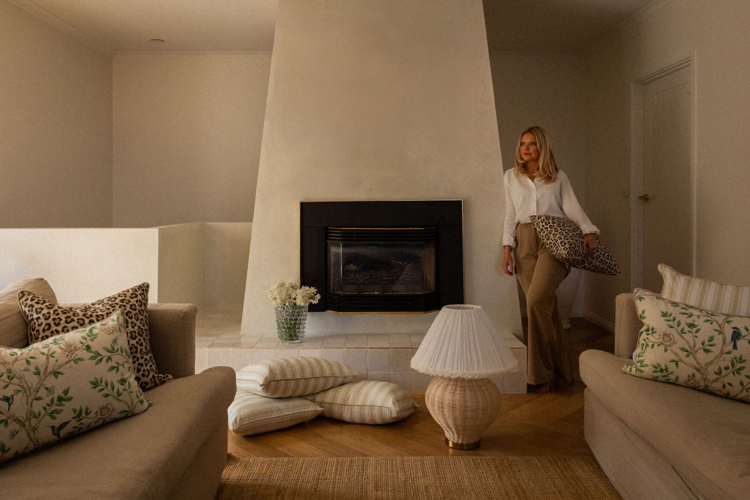 Cozy living room interior with fireplace, striped throw pillows, and natural jute rug in warm neutral tones.