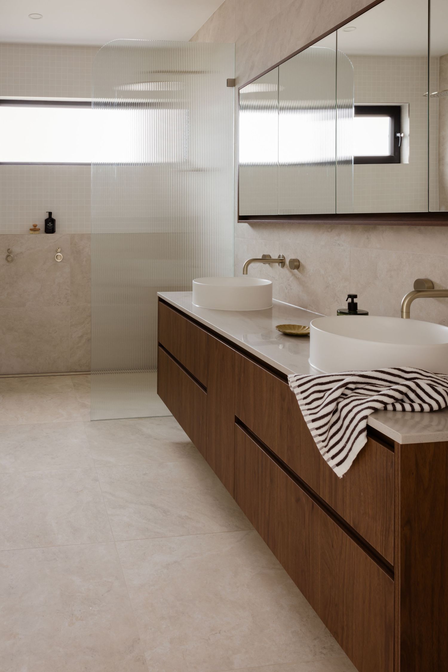 Modern minimalist bathroom featuring floating wooden vanity with dual vessel sinks and large mirror in neutral tones.