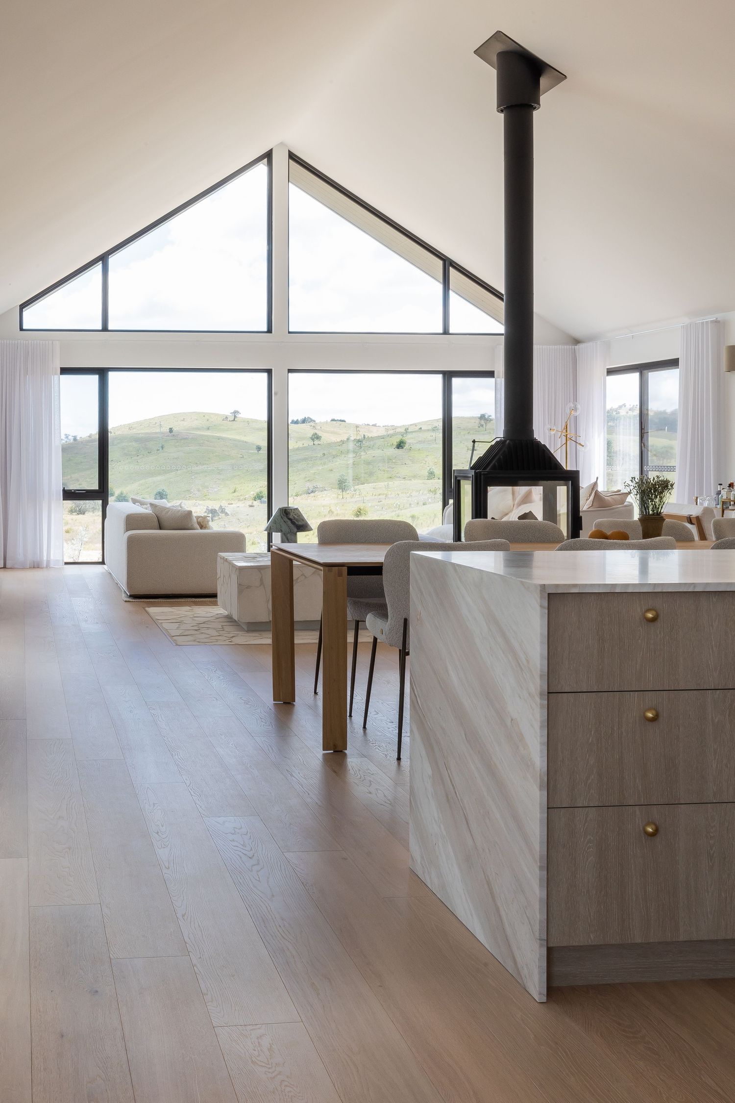 Modern farmhouse kitchen with vaulted ceiling and large windows overlooking rolling hills.