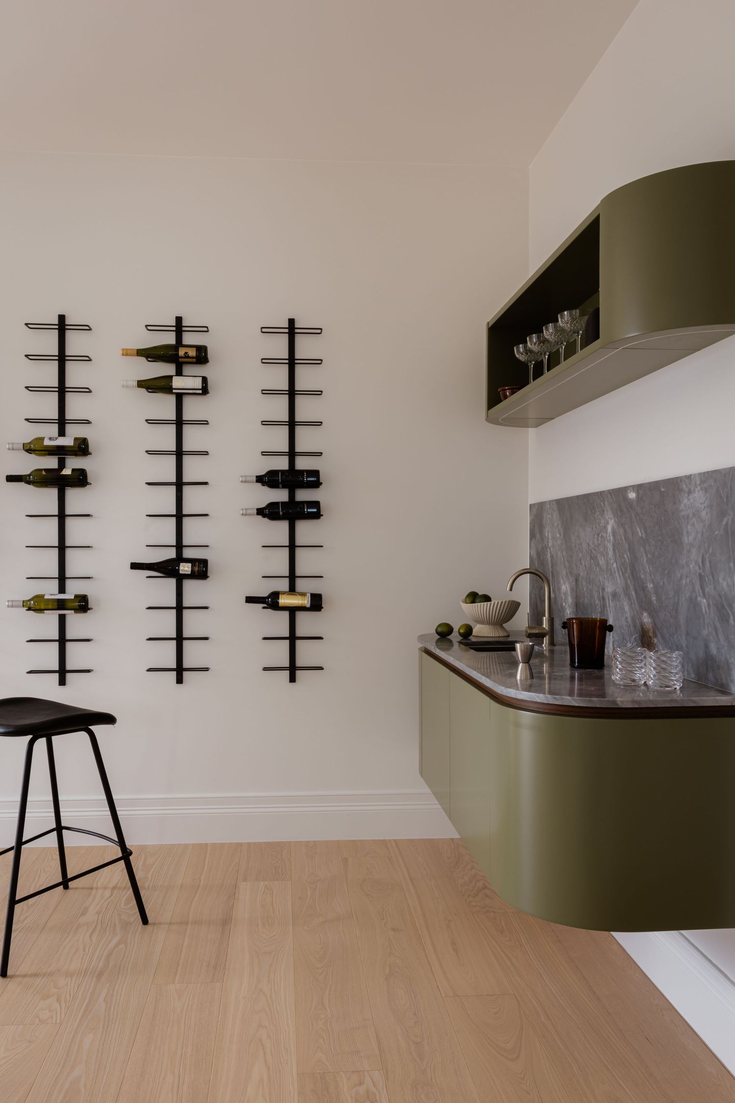 Contemporary wine bar area with vertical wall-mounted wine racks and olive green cabinetry.
