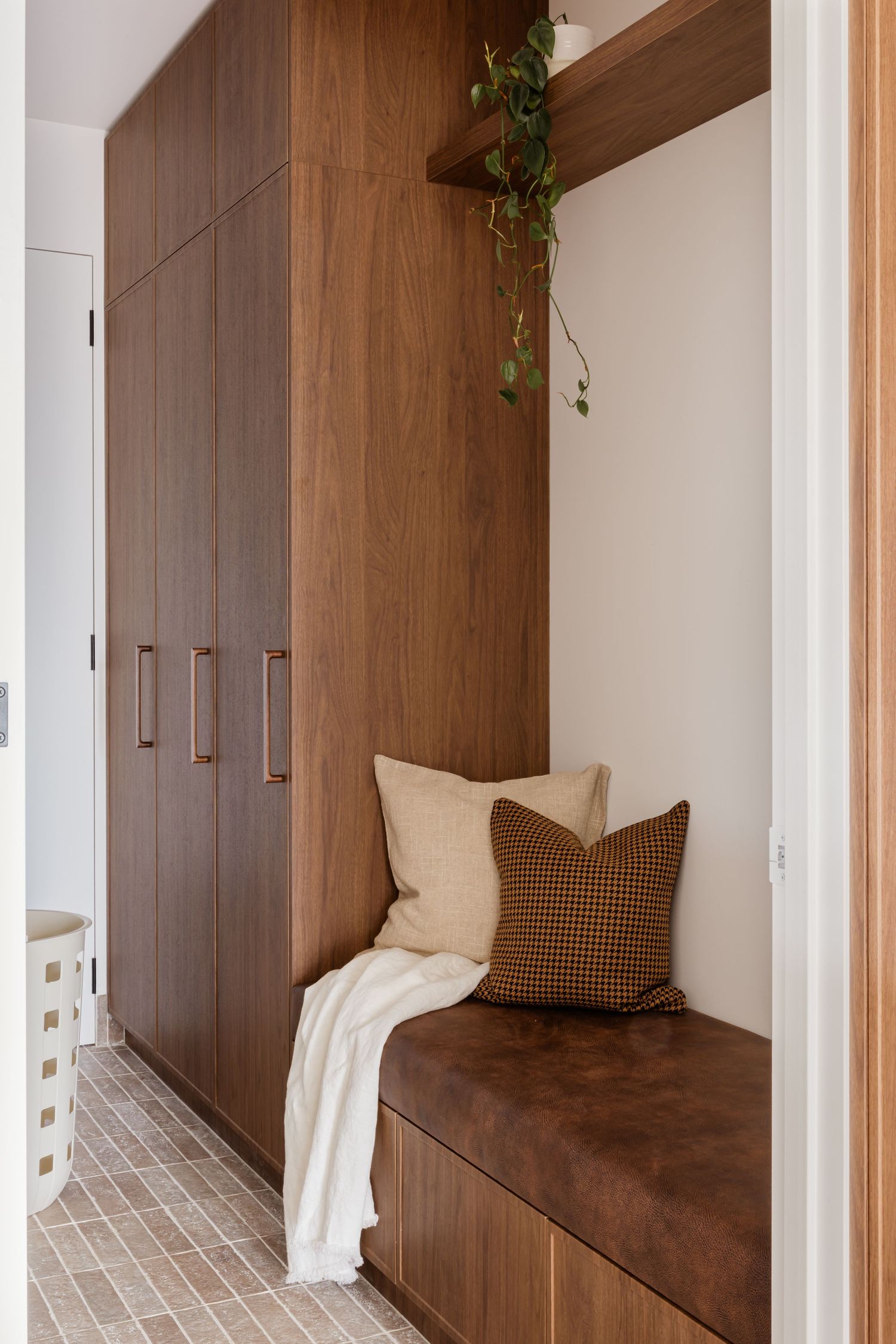 Built-in wooden entryway bench with storage cabinets and decorative pillows in warm brown tones.