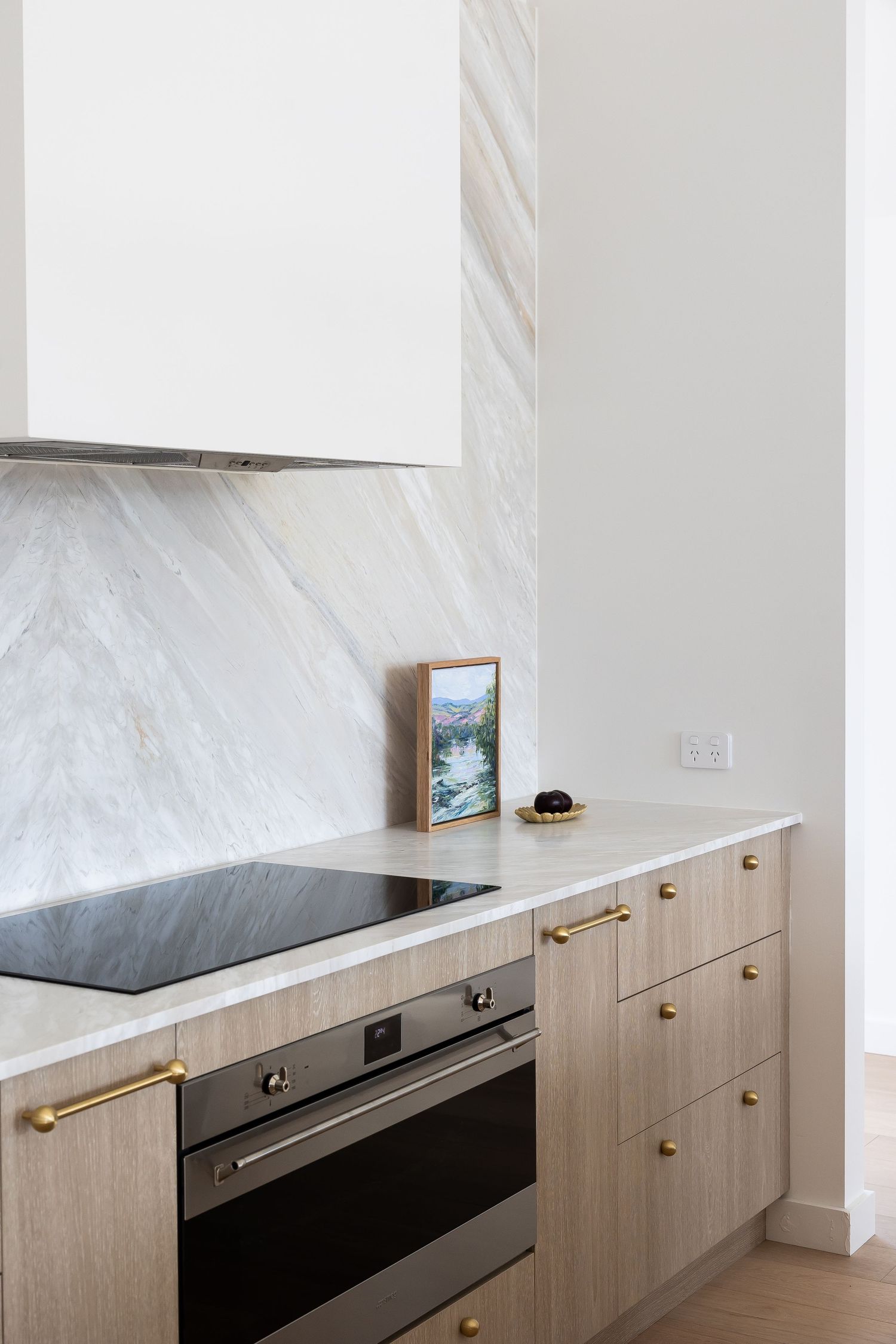 Modern kitchen design featuring light wood cabinets with brass handles and black appliances against a white marble backsplash.