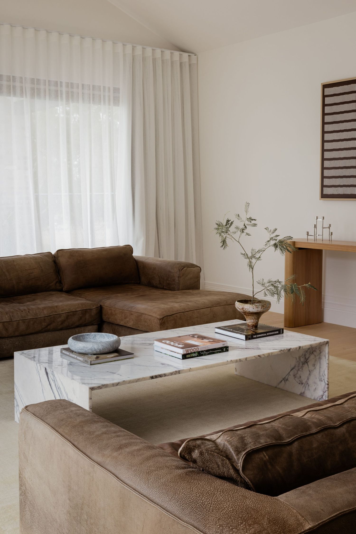 Minimalist living room interior with brown leather sectional sofa and marble coffee table against white walls.