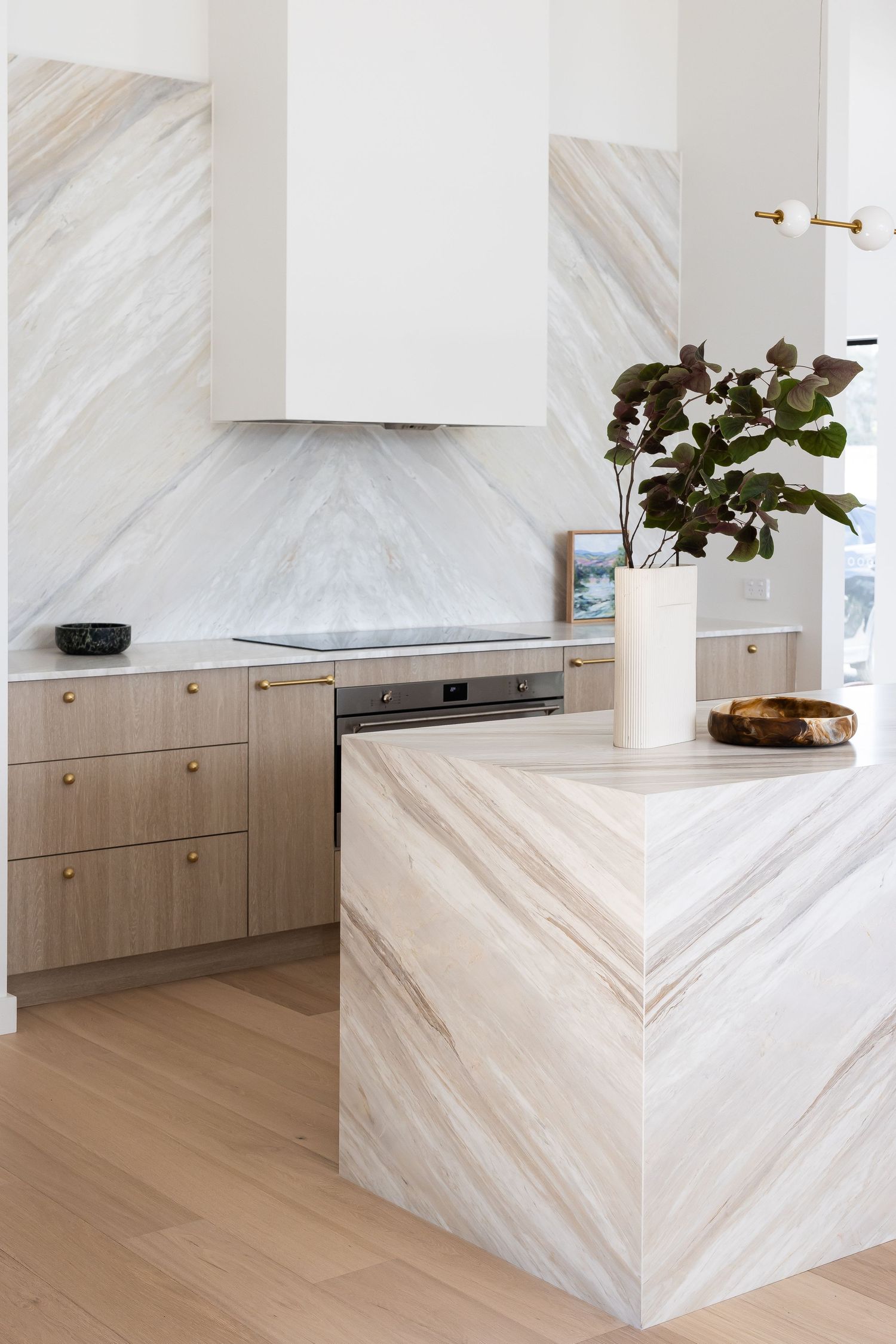 Contemporary kitchen featuring marble backsplash, light wood cabinetry, and chevron-patterned marble island.