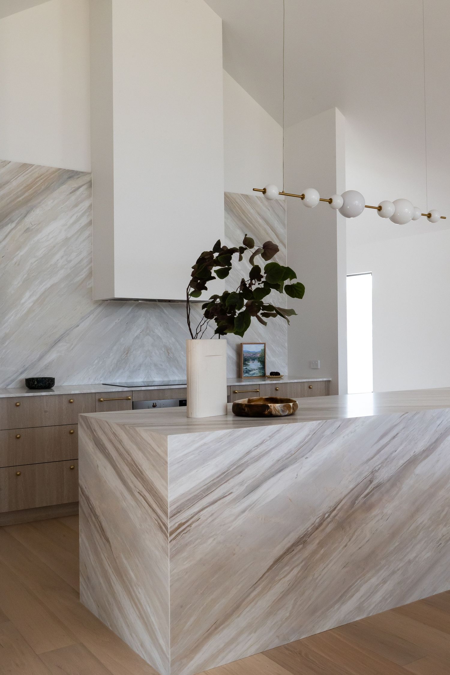 Contemporary kitchen featuring dramatic veined marble waterfall island and pendant lighting.