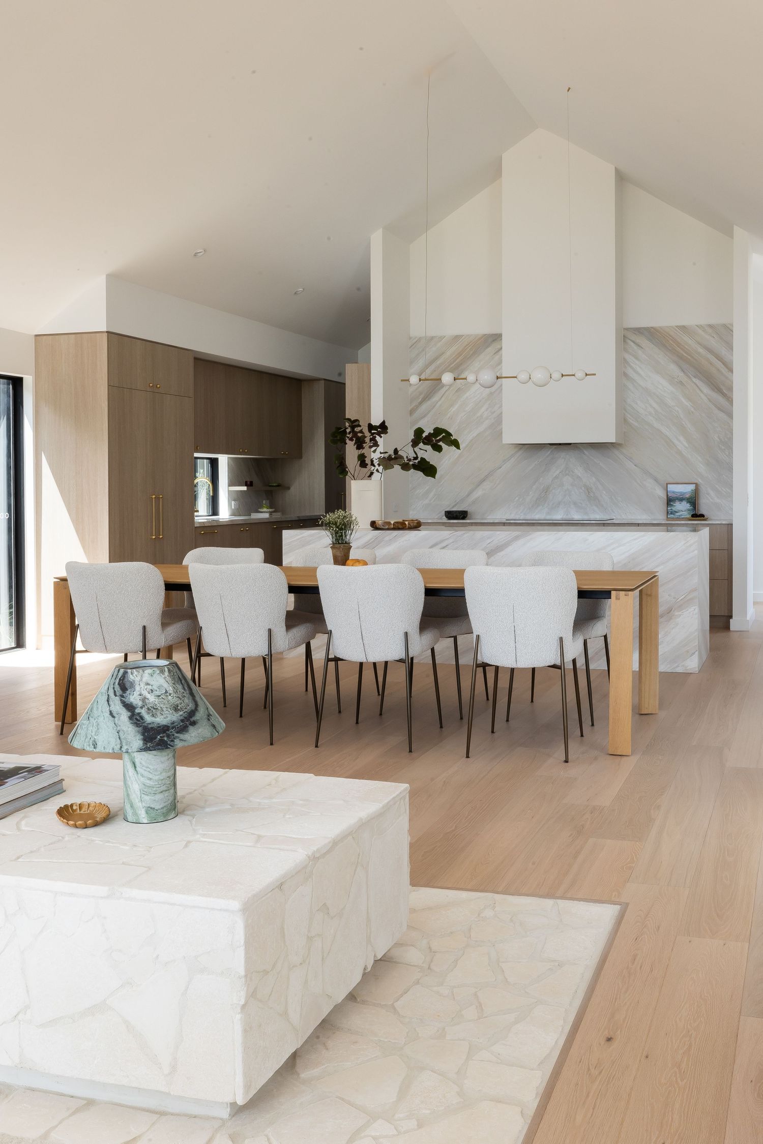 Elegant dining area with white upholstered chairs and marble kitchen island in modern open concept space.