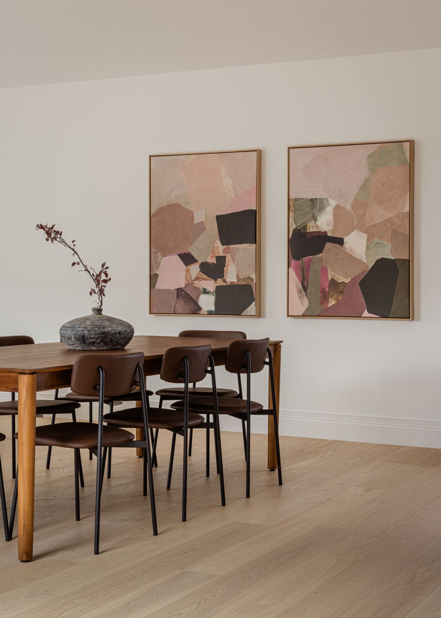 Contemporary dining room with wooden table, black chairs, and abstract pink and brown artwork on white walls.