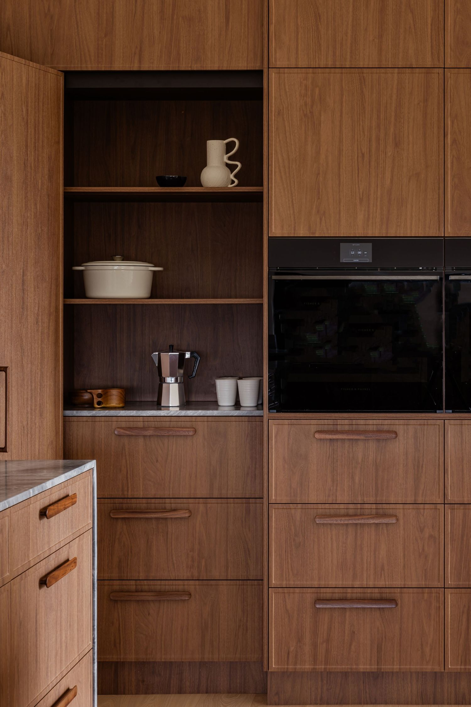 Built-in wooden kitchen cabinets with open shelving displaying stacked cups and cookware.