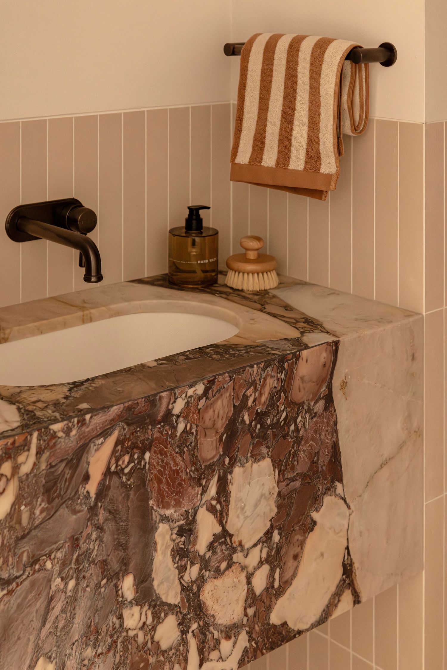 Luxurious marble bathroom vanity with wall-mounted faucet, striped towel, bath accessories on beige tiled wall. Canberra interior Photograph