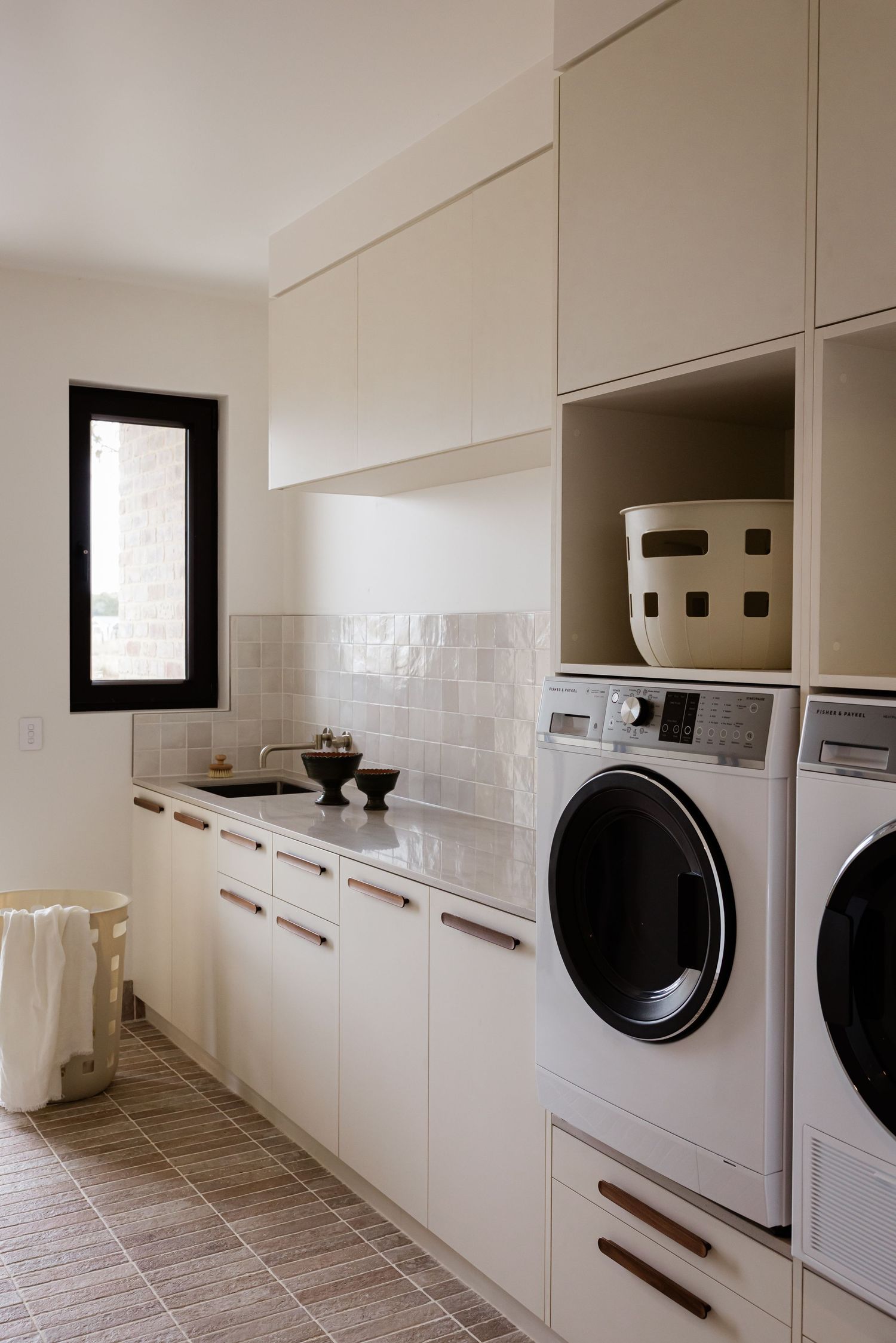 Modern laundry room with white cabinetry, dark front-loading washer and dryer, and neutral tile flooring.