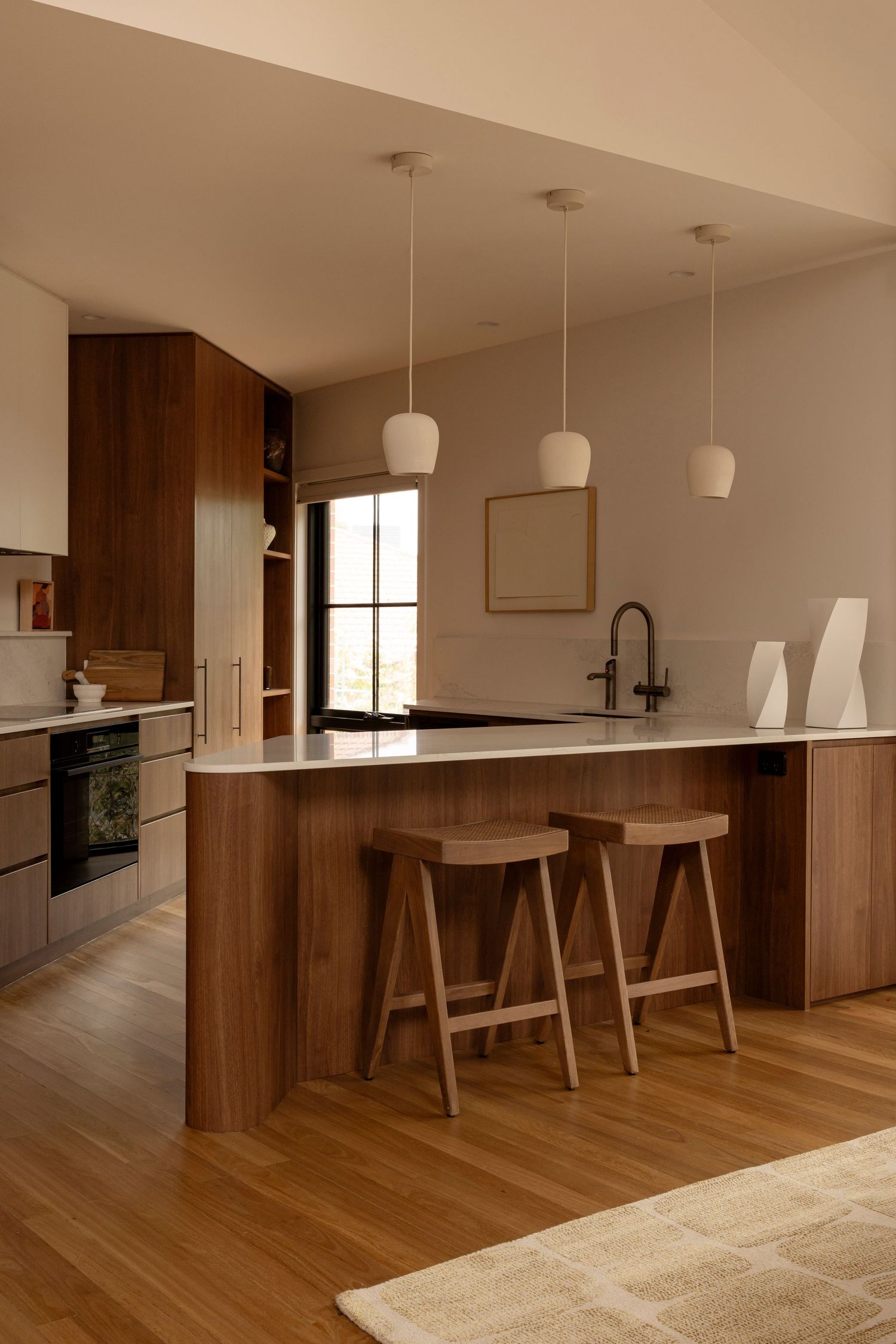 Modern minimalist kitchen with wooden cabinets, white countertops, and pendant lights features a sleek breakfast bar.