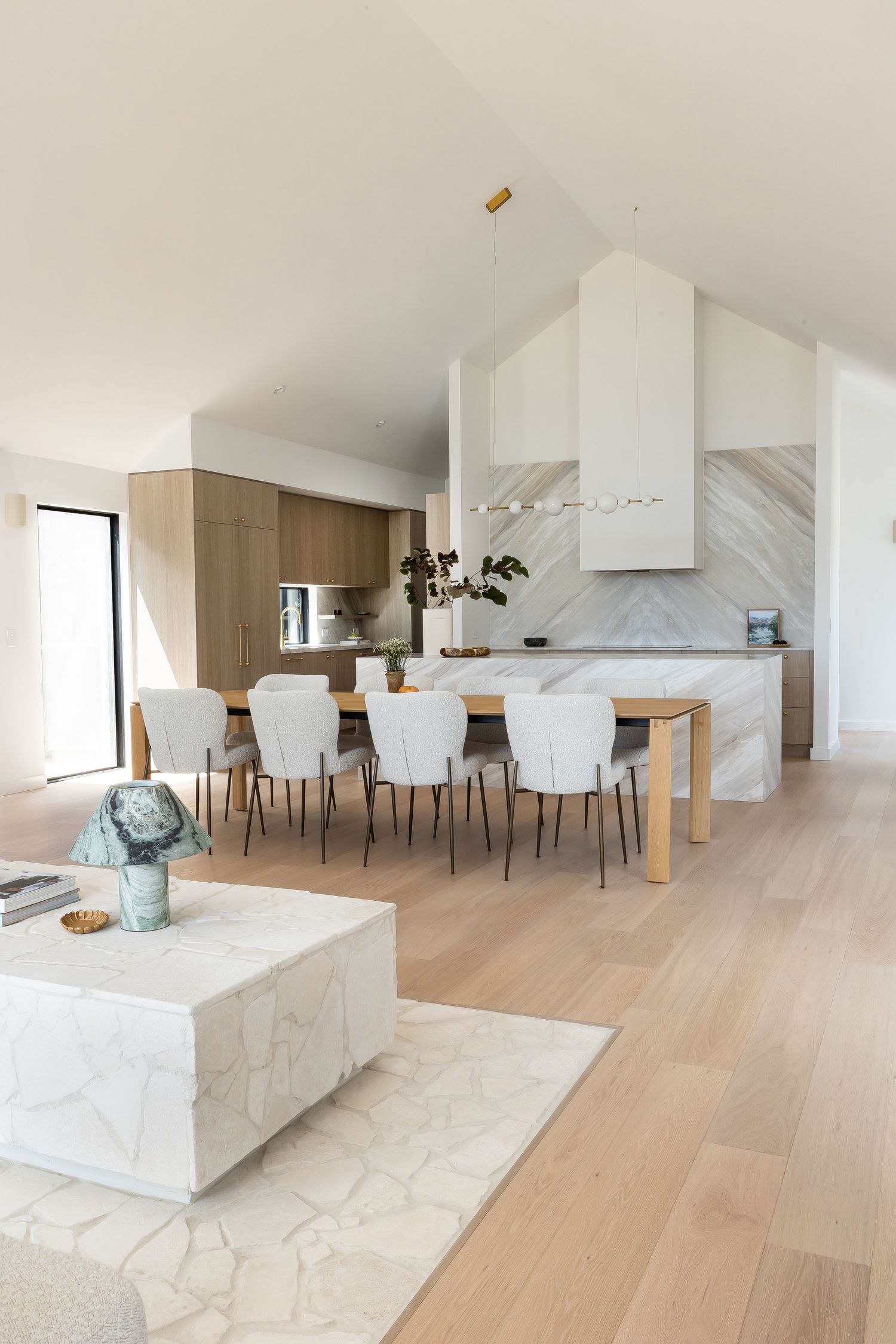 Contemporary open concept dining area with marble features, white chairs, and wooden floors in natural lighting.