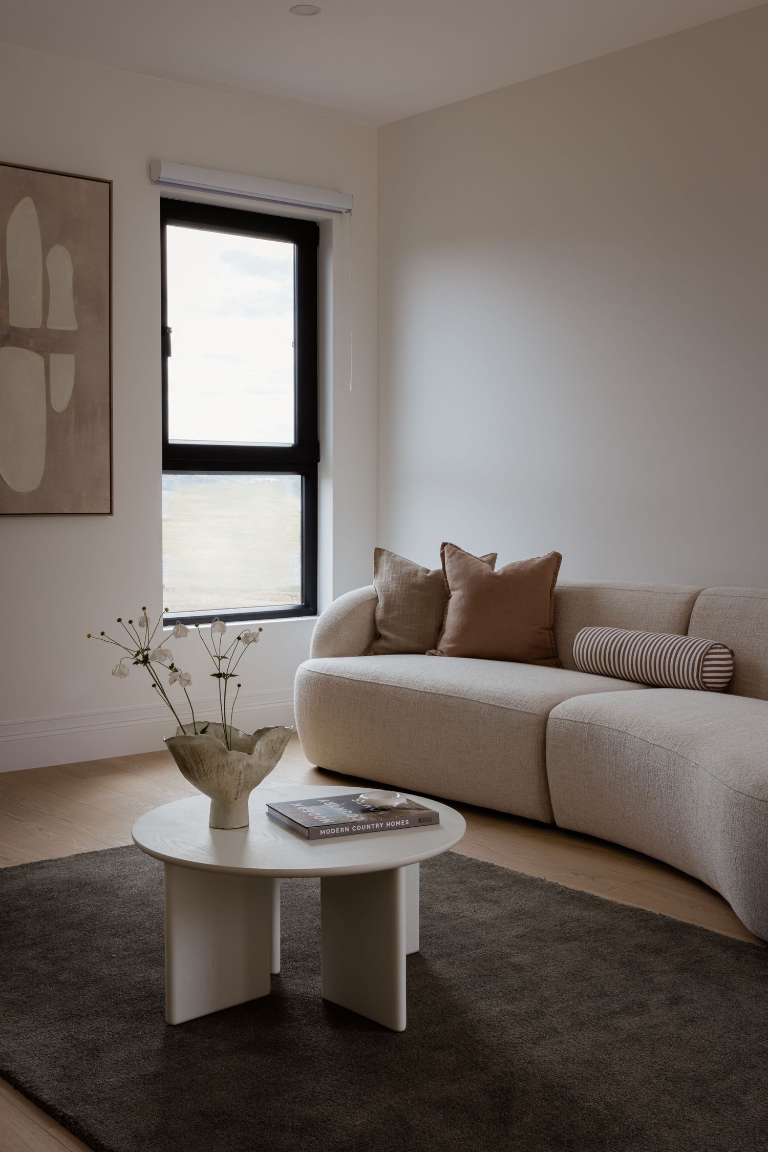 Minimalist living room with curved beige sofa, white round coffee table, and modern wall art.