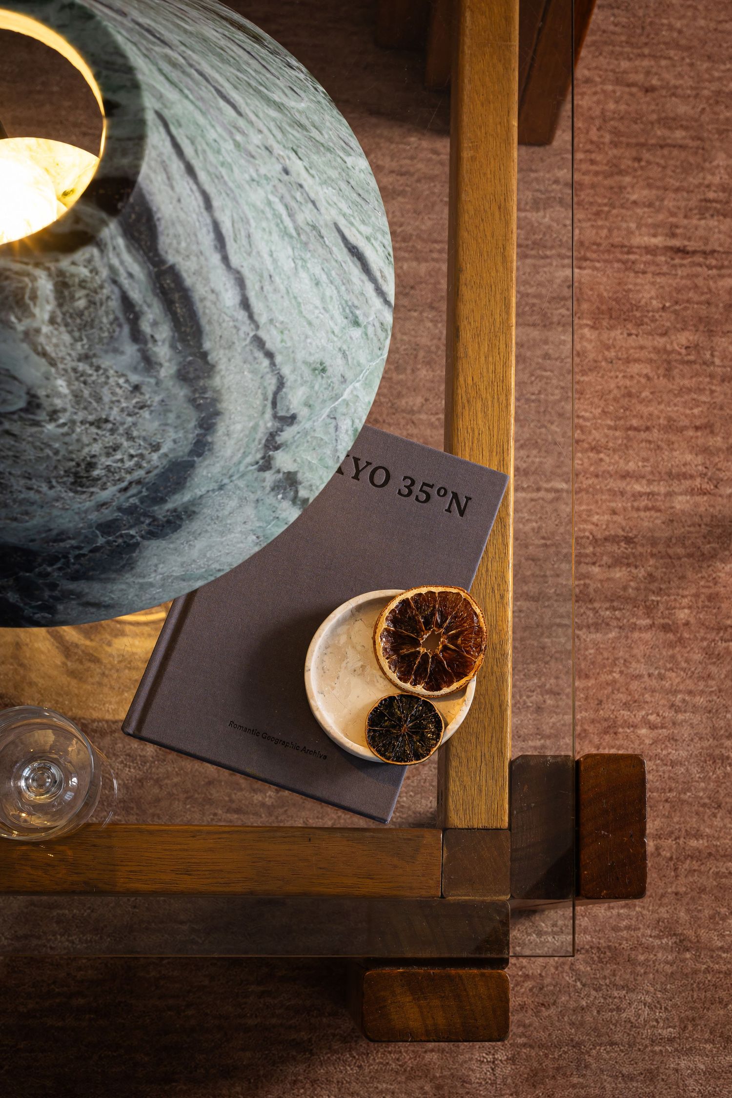 Moody still life with stone lamp, dark book, and dried citrus slices on wooden surface.