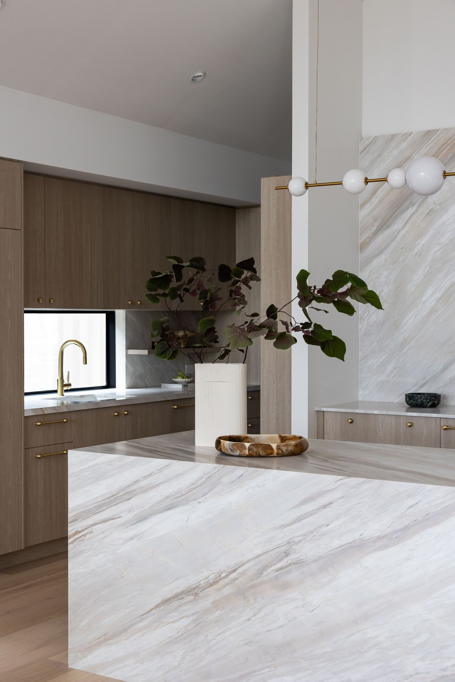 Modern kitchen with luxurious marble waterfall island, wooden cabinets, and minimalist white pendant lights.