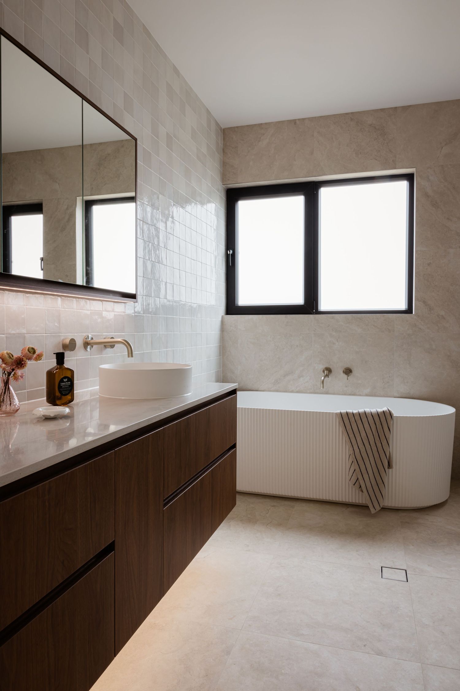 Modern bathroom interior with floating wooden vanity, freestanding tub, and large mirror in neutral beige tones.