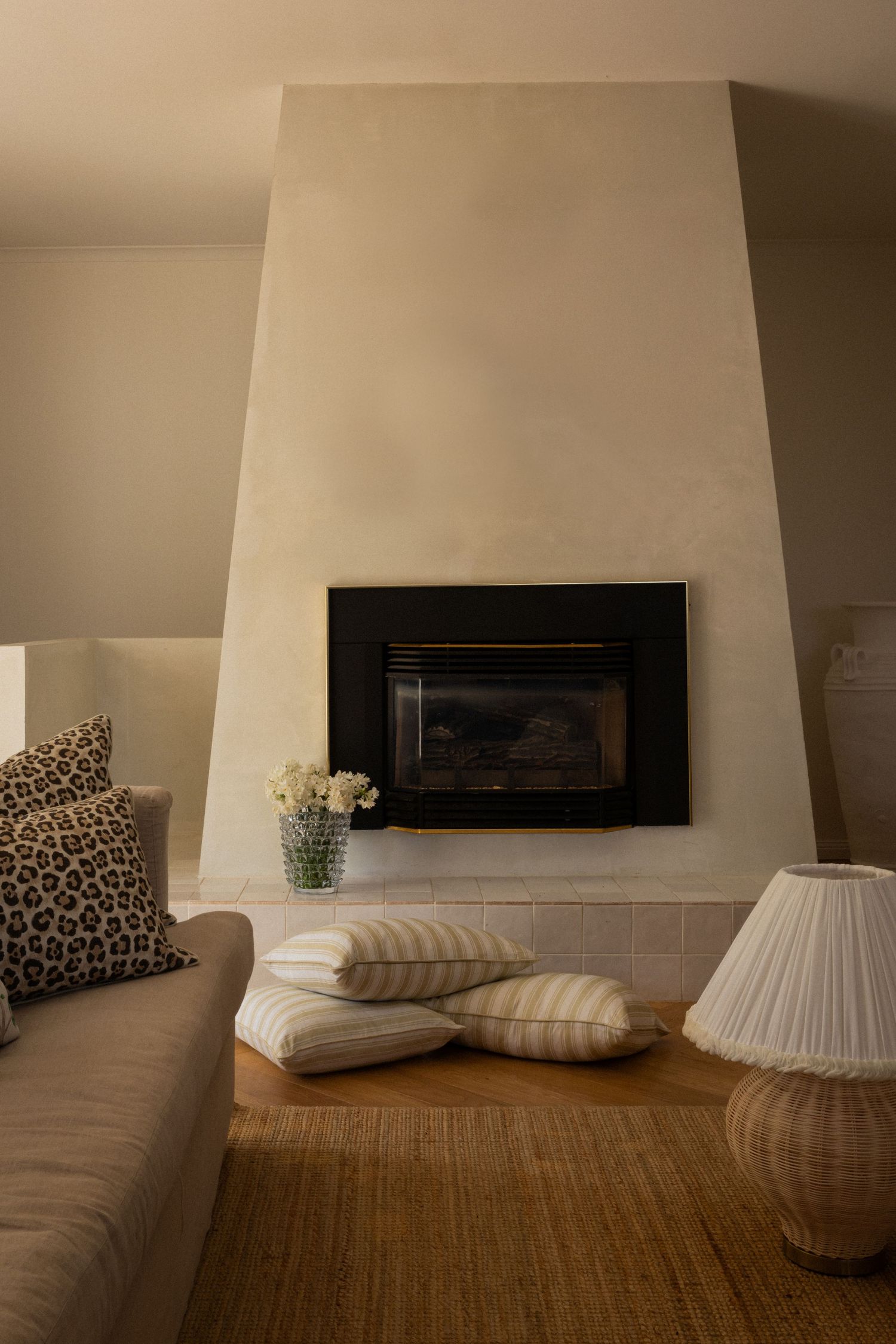 Modern minimalist fireplace with beige walls, leopard print pillows, and table lamps on natural fiber rug.