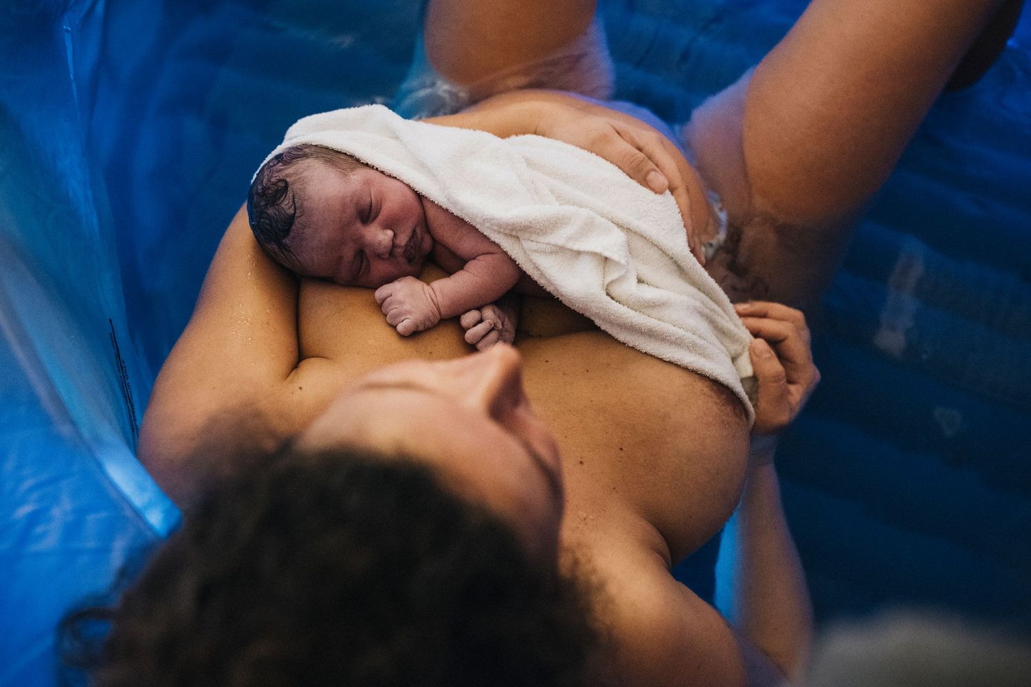 Birth scene in a blue pool with gentle lighting.