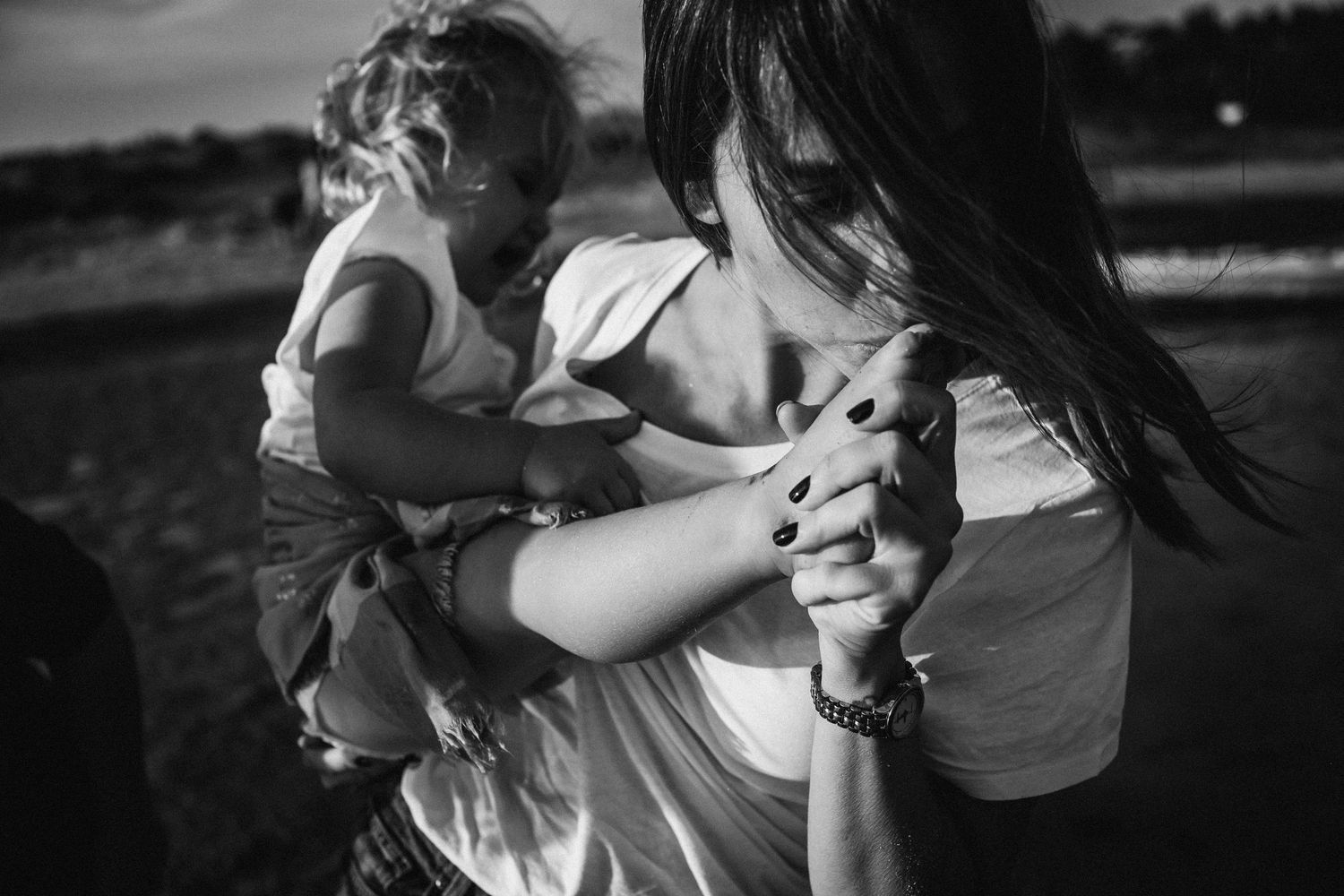 Black and white candid photograph of a tender moment between parent and child outdoors in natural light.