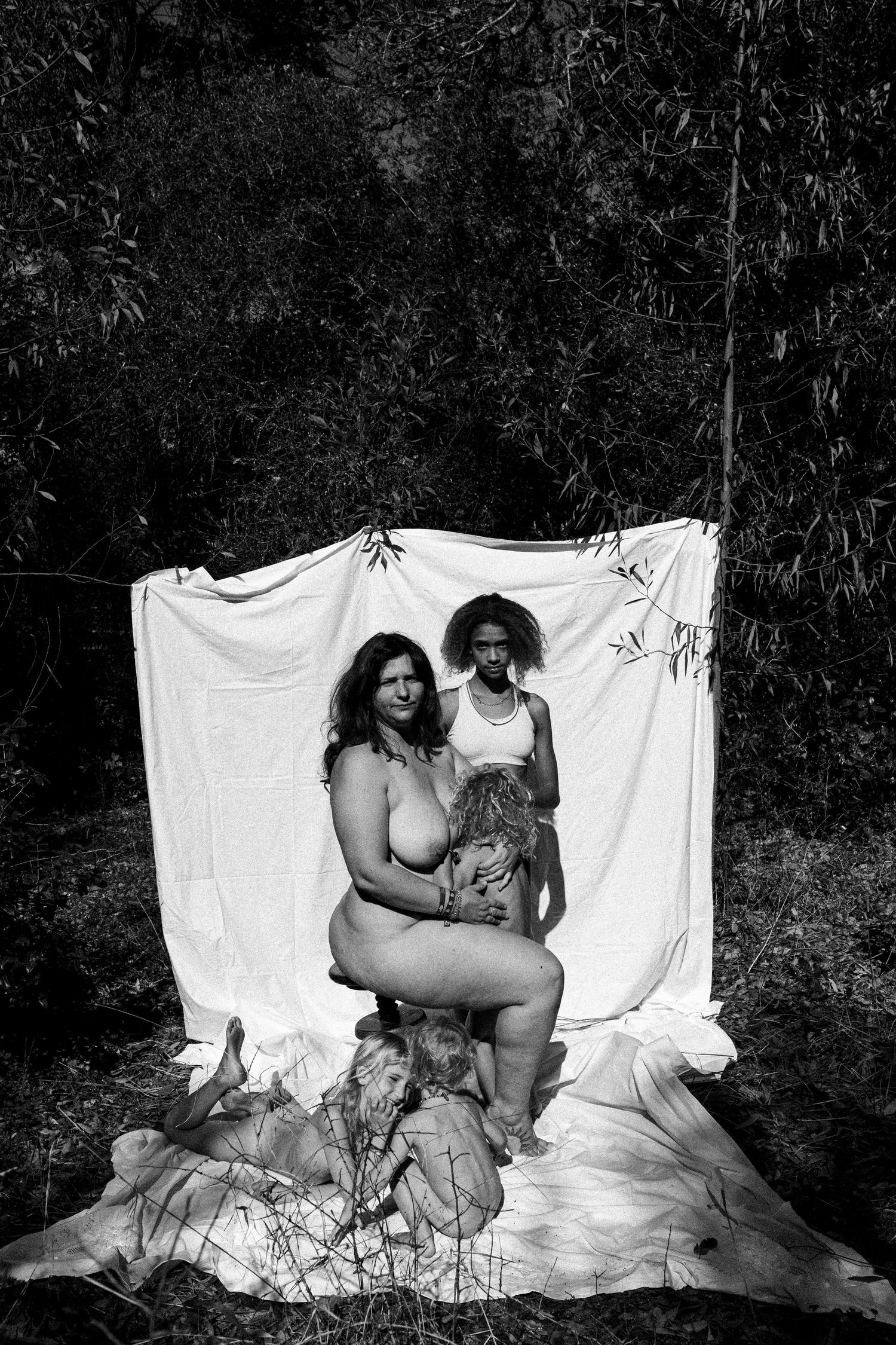 A series of black and white artistic nude photographs taken against a white backdrop in a natural outdoor setting.